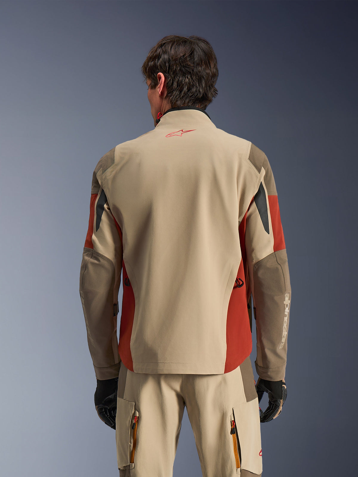 Homme portant la veste d'aventure Alpinestars Maxdura Drystar®XF Laminated Armored Shell vue de dos, coloris Aluminum Walnut et Rust Brown, avec pantalon technique assorti et gants noirs, construction textile laminée 3 couches avec panneaux renforcés, tenue coordonnée pour le touring moto