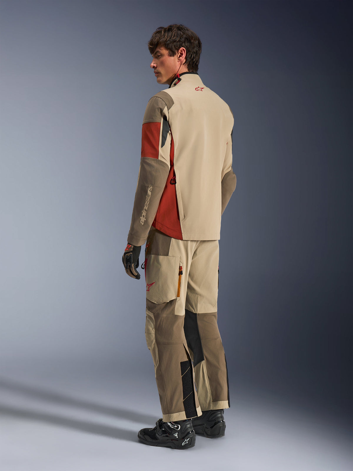 Mannequin homme portant la veste Alpinestars Maxdura Drystar®XF Laminated Armored Shell en Aluminum Walnut Rust Brown, pantalon d'aventure touring assorti, gants noirs et bottes noires, vue de dos montrant la construction textile technique et les zones renforcées.