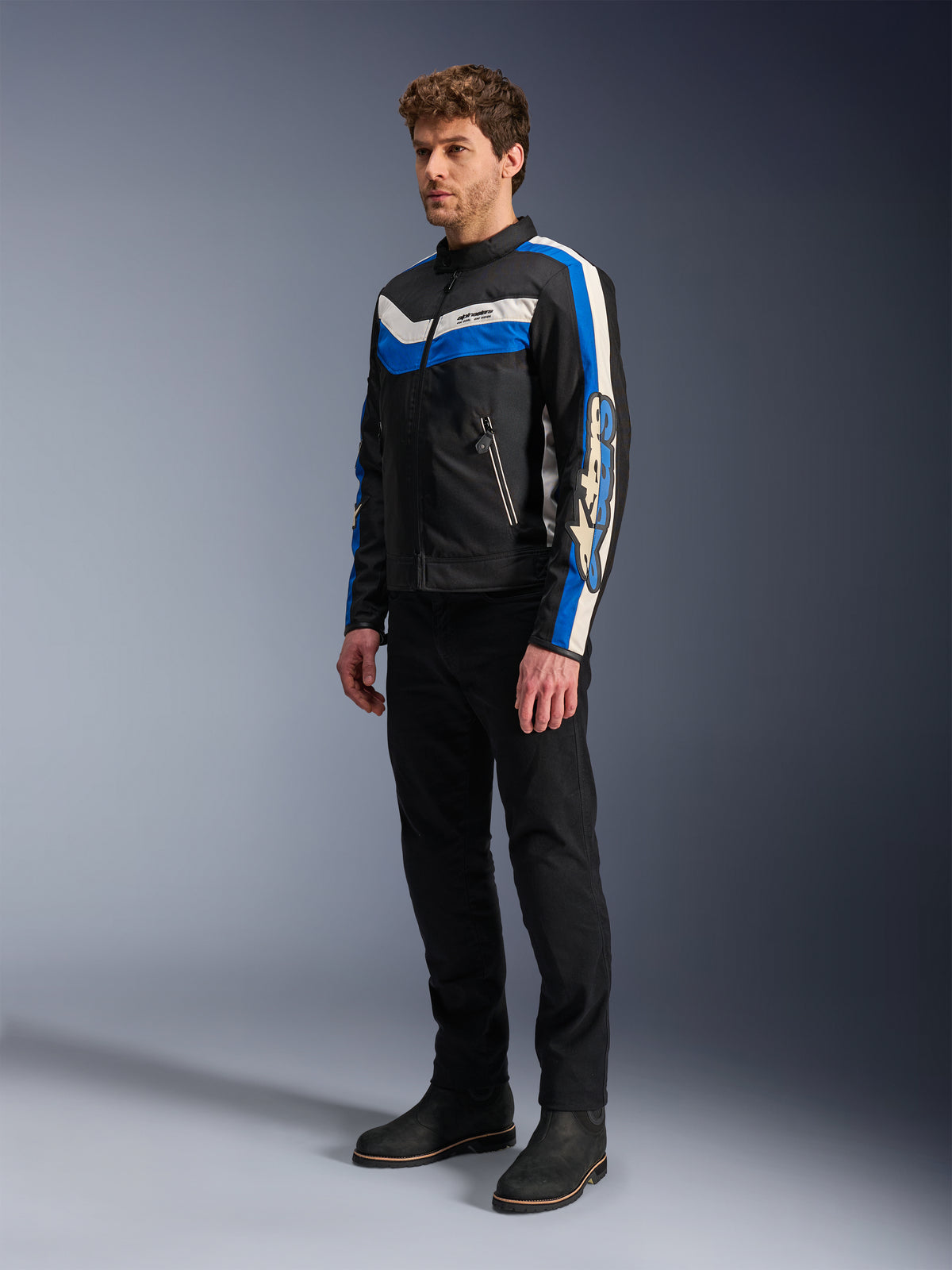 Veste Alpinestars T-Dyno WR, noir, bleu et écru, veste de moto en textile portée par un mannequin avec un pantalon noir et des bottes, design d'inspiration vintage avec des rayures bleues et écrues et marquage sur les manches, photographie de studio