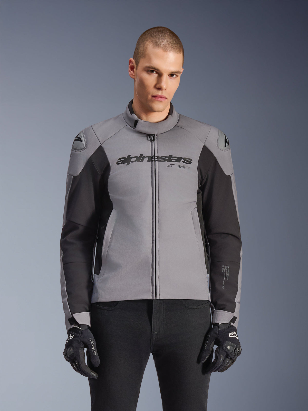 Alpinestars SMX Waterproof Jacket, veste de moto de route sportive, gris foncé et noir, avec un col montant et des sliders d'épaule DFS Lite, portée avec des gants SMX noirs, coupe athlétique élégante pour rouler par tous les temps