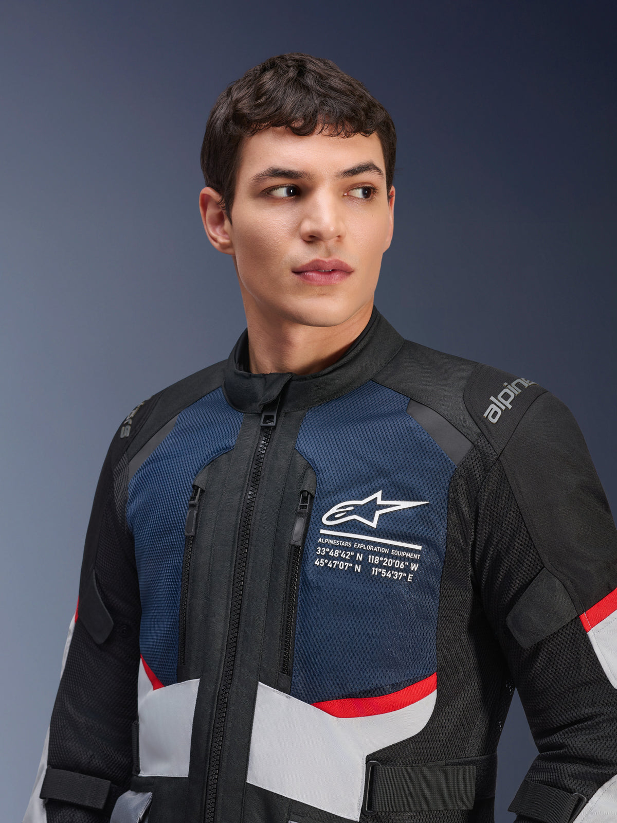 Veste Alpinestars Andes Air Drystar®, veste de moto, bleu foncé, noir et gris glace avec des accents rouges, portée par un mannequin homme, avec panneaux de poitrine en mesh ventilé, logo étoile blanche avec coordonnées d'exploration, et design d'aventure prêt pour la route