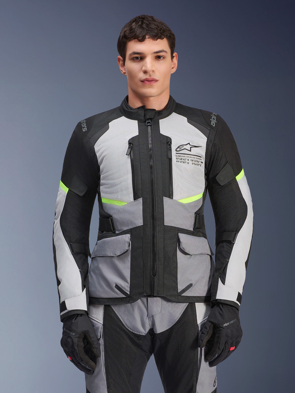 Veste Alpinestars Andes Air Drystar, veste de moto touring, gris glace et gris foncé avec empiècements noirs et détails jaune fluo, portée avec un pantalon et des gants assortis, dotée de panneaux de ventilation en mesh et de poches cargo