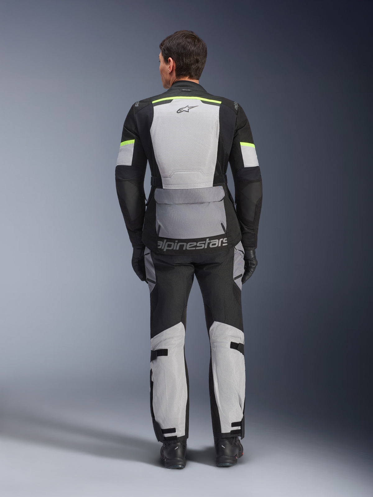 Ensemble veste et pantalon Alpinestars Andes Air Drystar®, tenue de touring aventure Ice Gray Dark Gray Black, vue arrière d'un pilote portant l'équipement complet avec accents jaune fluo, doté de larges panneaux de ventilation en mesh et du marquage Alpinestars