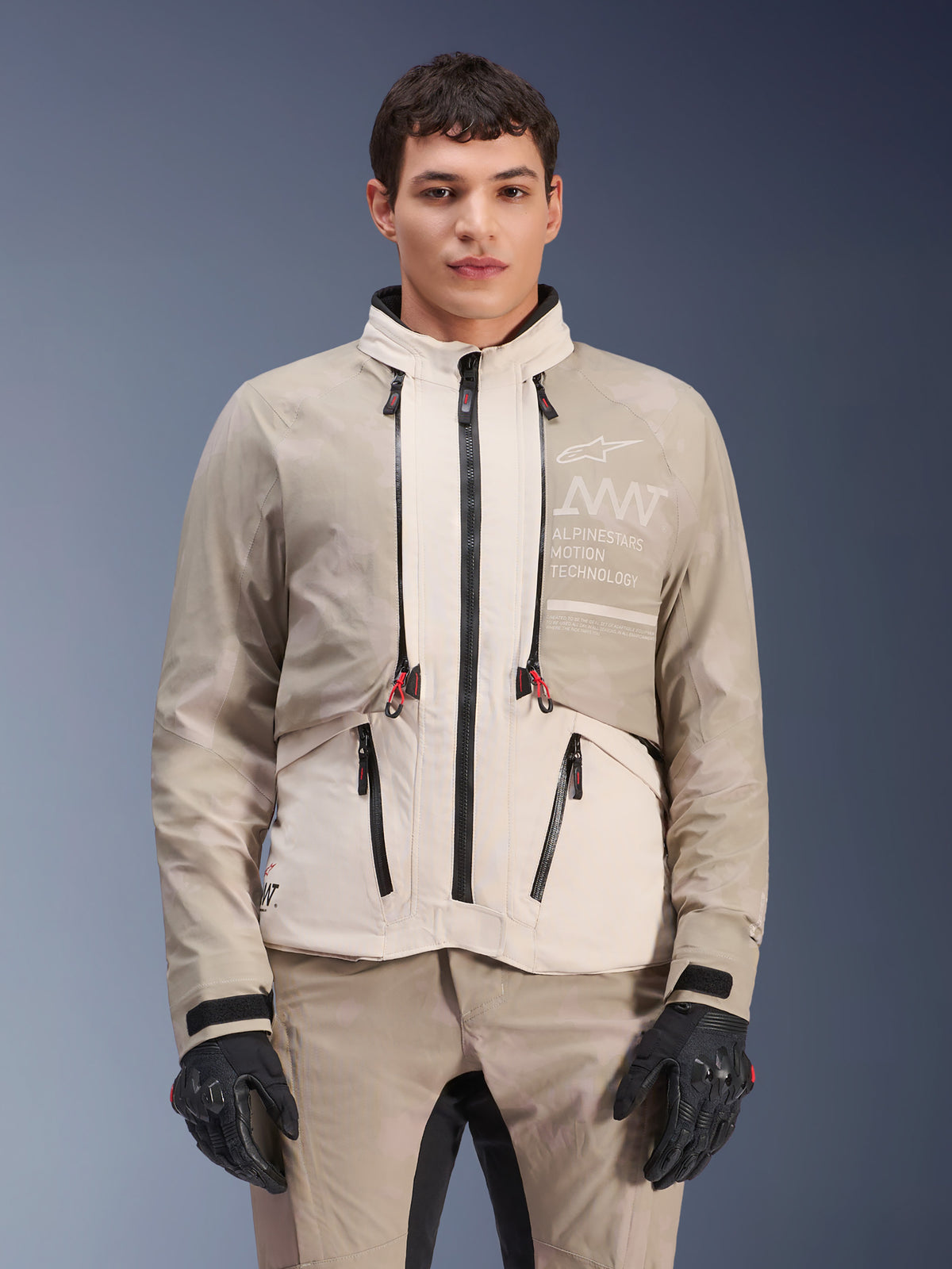 Veste Alpinestars AMT-10LAB Drystar® XF, veste de moto d'aventure, White Sand Aluminum Camo, design modulaire avec fermetures éclair noires et accents rouges, portée avec un pantalon assorti et des gants noirs, avec le marquage Alpinestars Motion Technology sur la poitrine, tenue de moto professionnelle toutes saisons