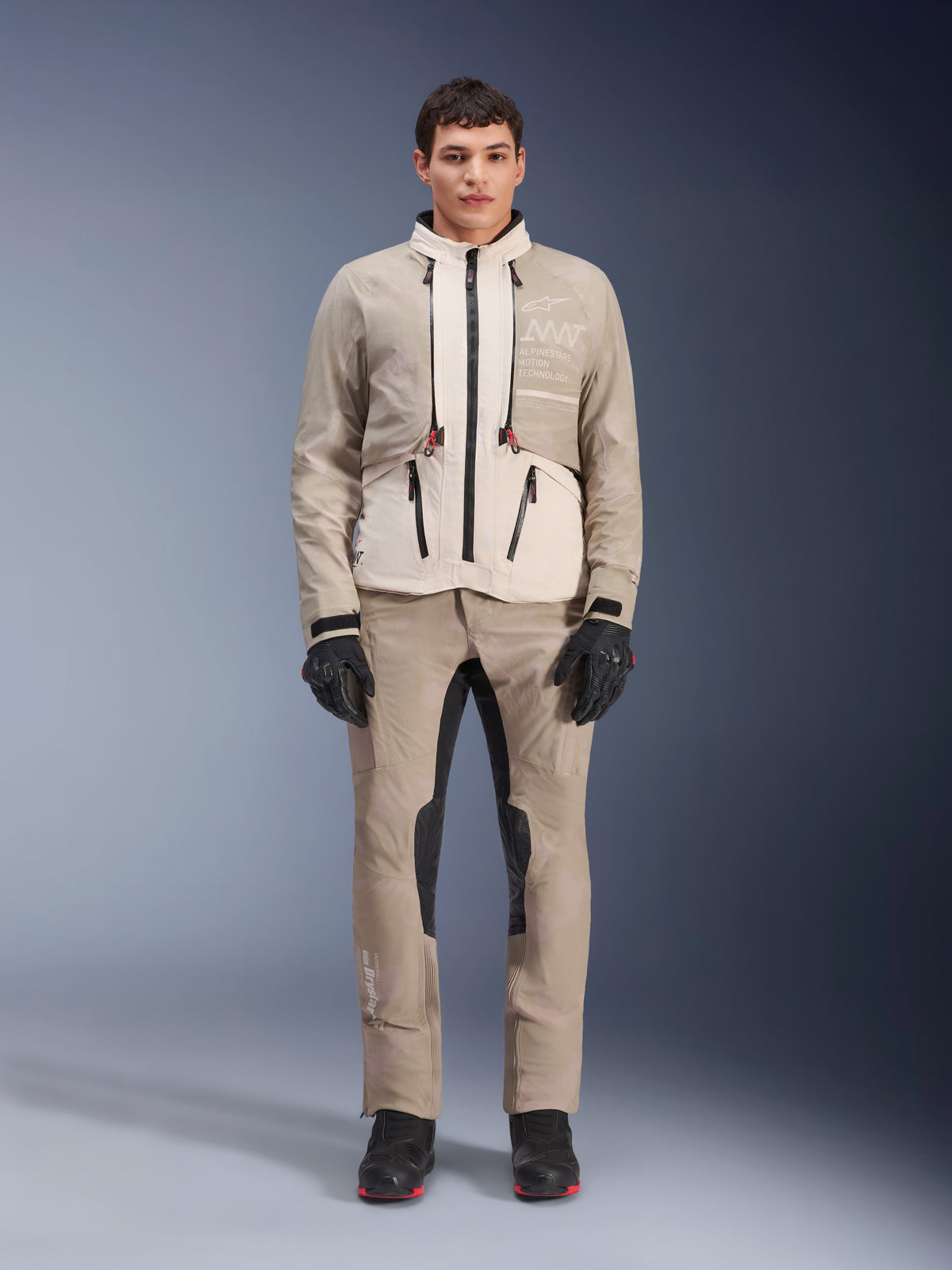 Veste Alpinestars AMT-10LAB Drystar® XF en White Sand Aluminum Camo, portée par un mannequin avec un pantalon d'aventure assorti, des gants noirs et des bottes noires, équipement de moto technique modulaire pour le touring multi-saison.