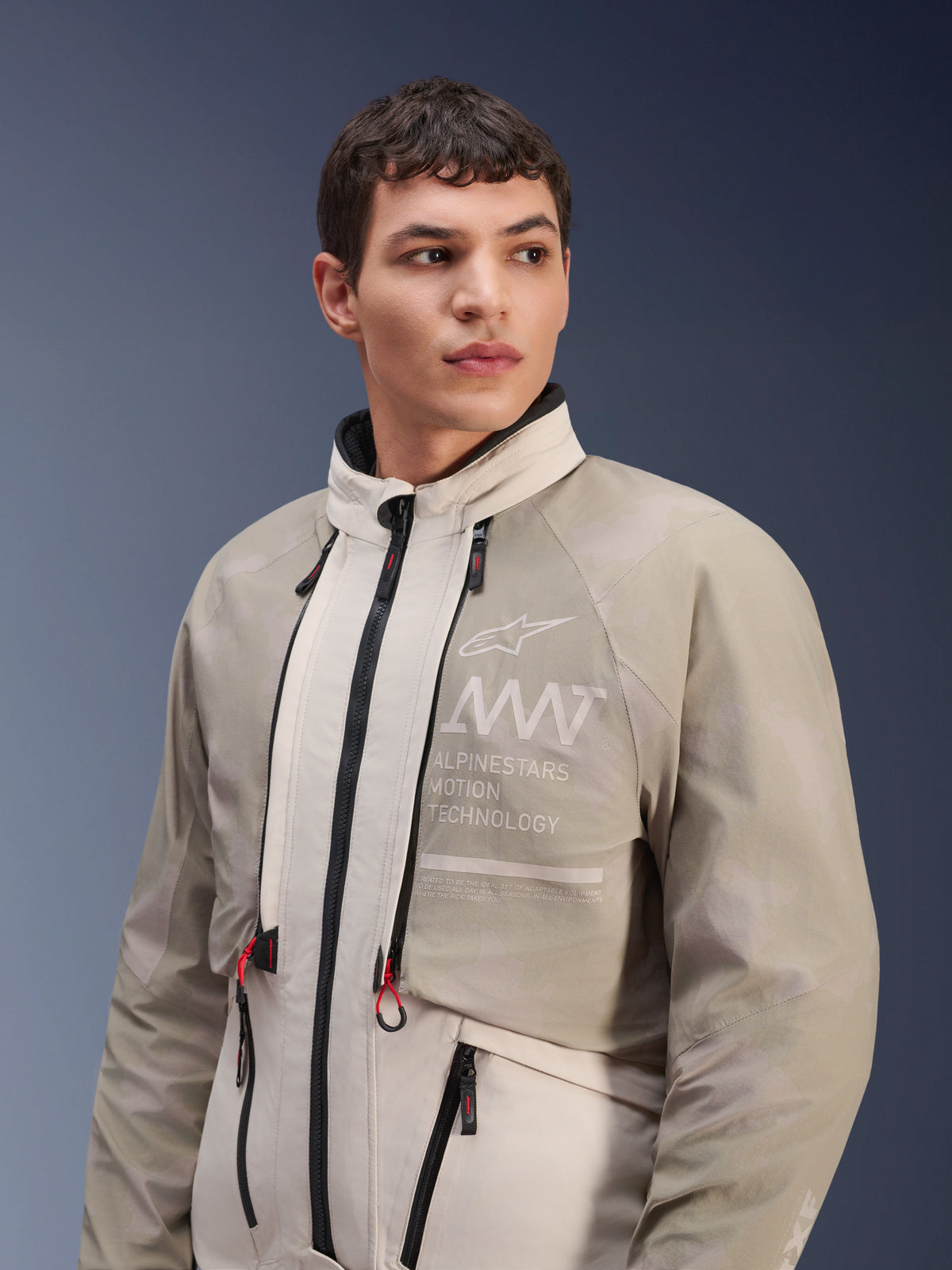 Veste Alpinestars AMT-10LAB Drystar® XF, White Sand Aluminum Camo, veste de moto d'aventure modulaire, avec le marquage « Alpinestars Motion Technology » sur la poitrine, portée par un mannequin homme.