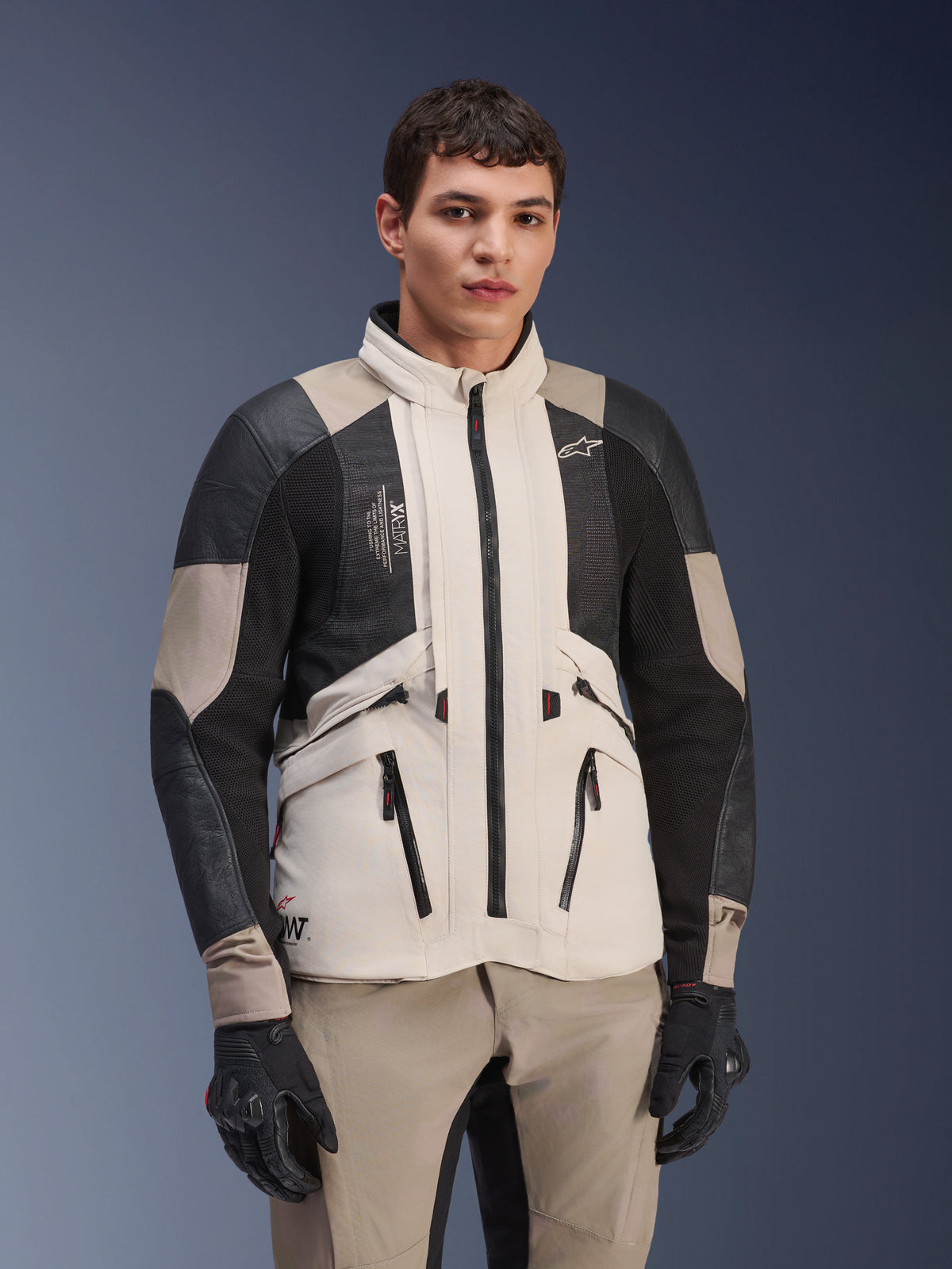 Veste Alpinestars AMT-10LAB Drystar® XF, White Sand Aluminum Camo, veste de moto d'aventure avec panneaux en maille MATRYX® noirs et renforts en cuir, portée par un mannequin avec gants noirs et pantalon sable assorti, portrait en studio