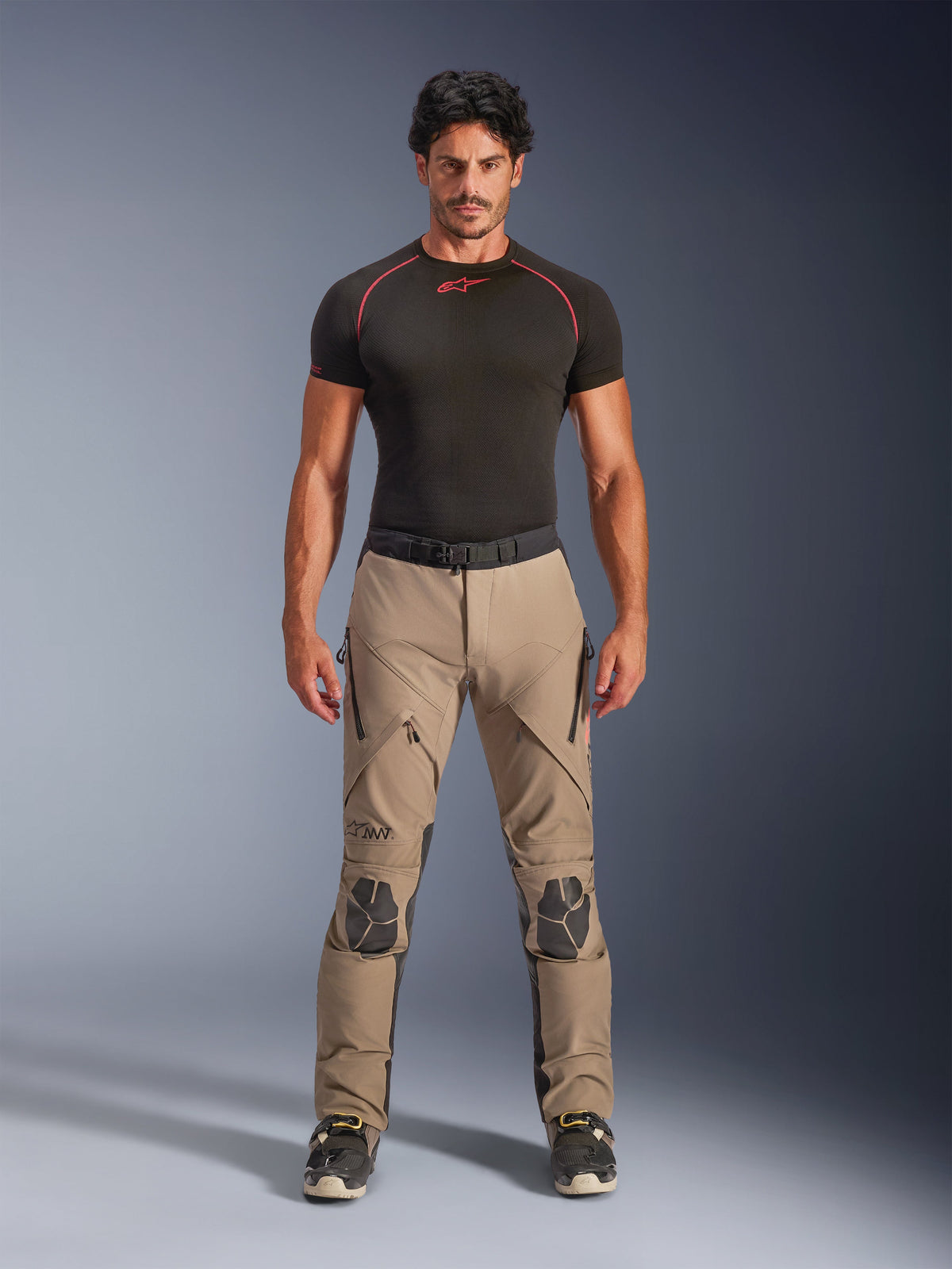 Mannequin homme portant le pantalon Alpinestars AMT-8 Stretch Drystar® XF en Walnut et Black, associé à une couche de base noire à manches courtes, pantalon d'aventure touring doté de genoux renforcés, de ventilations zippées et d'une conception extensible ergonomique.