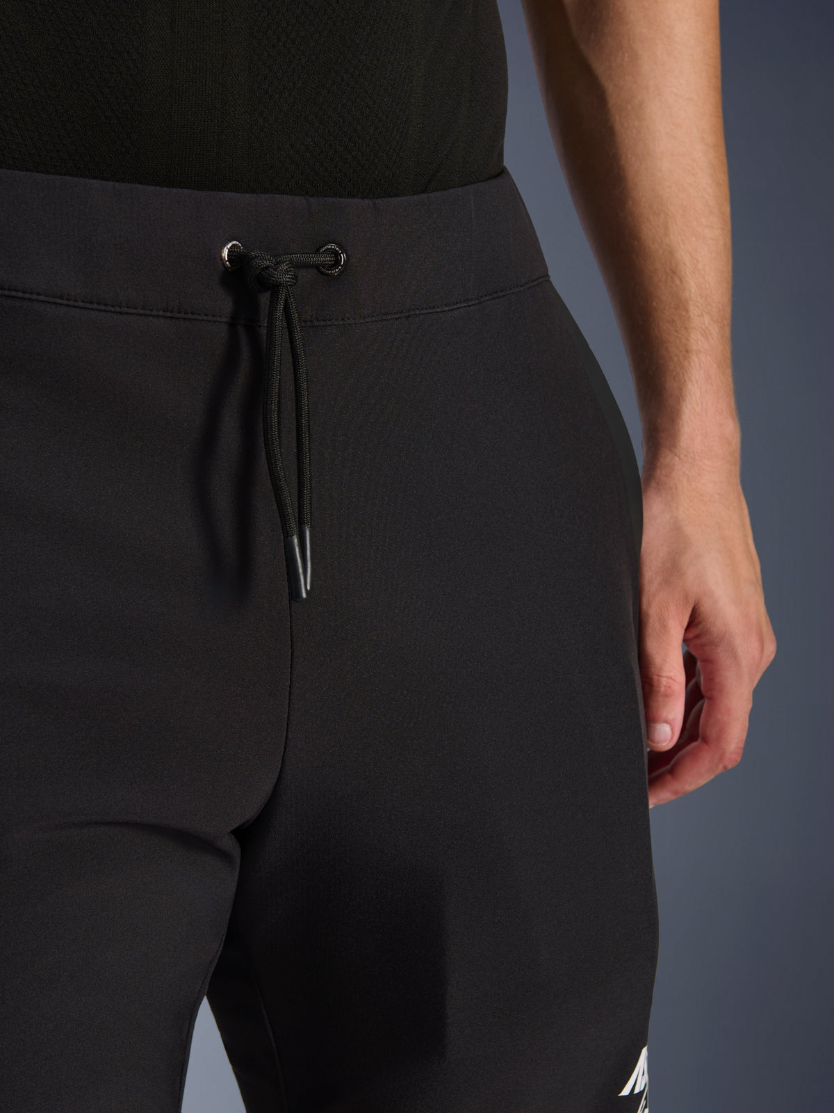 Pantalon Alpinestars Aeroshell, pantalon de moto en softshell noir, vue rapprochée de la taille élastique et du cordon de serrage, design minimaliste moderne, construction textile durable pour le touring décontracté