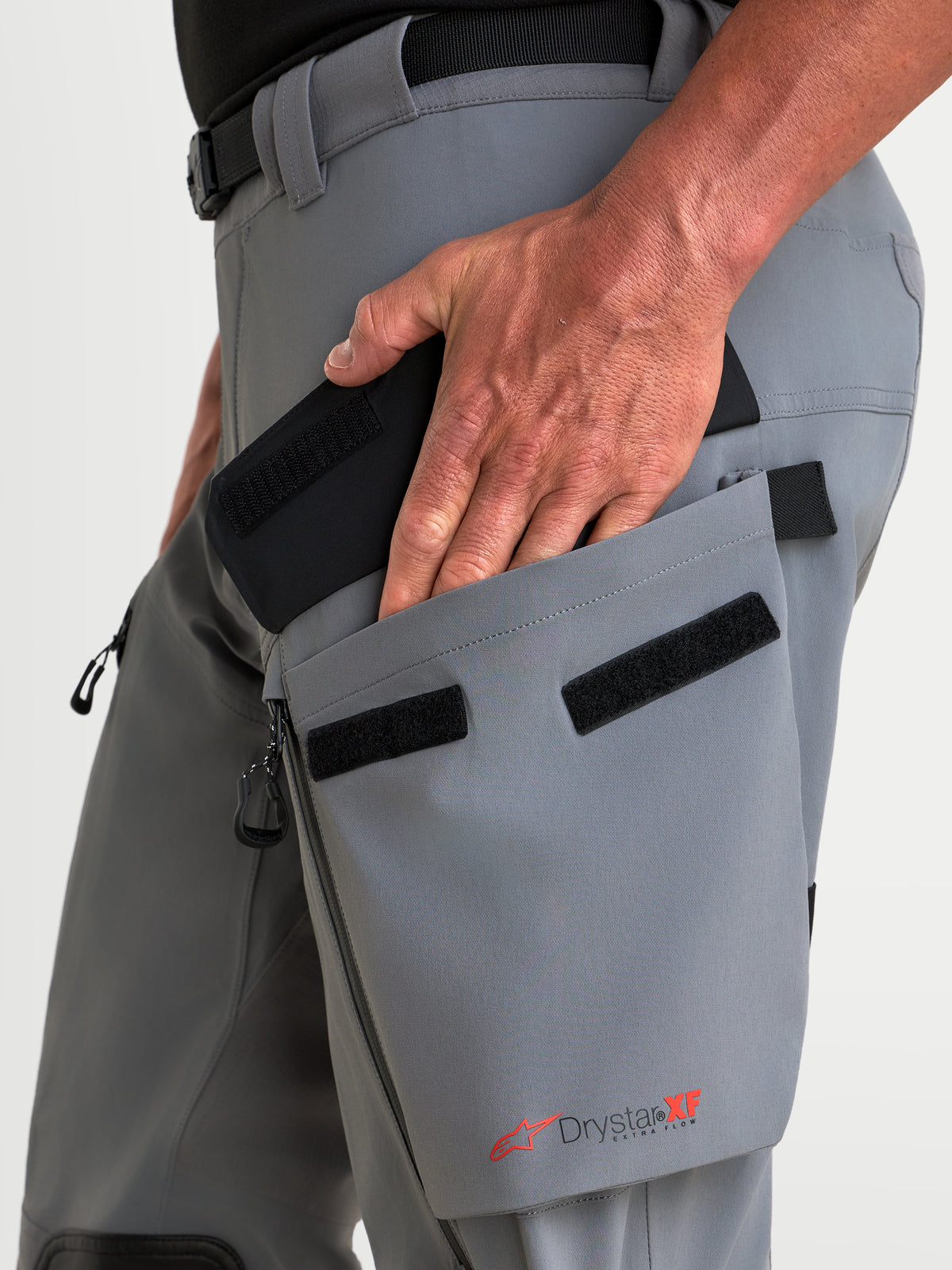 Alpinestars Maxdura Drystar XF Laminated Pantalons, pantalon de moto adventure gris foncé et noir, avec une main accédant à la poche cargo inclinée sur la cuisse et le marquage Drystar XF