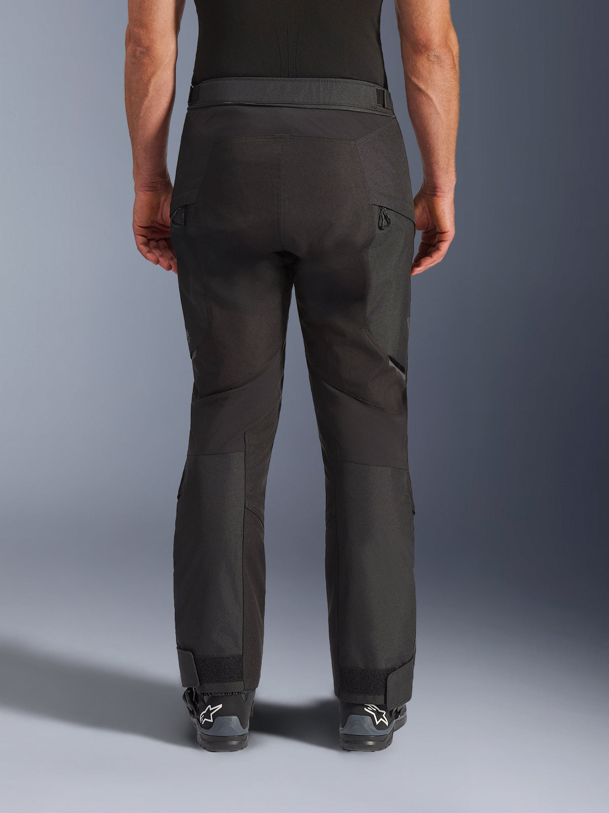 Alpinestars Cusco Drystar® Pants, Motorcycle Pants, Black, rear view worn by a rider, featuring textured textile panels, zippered vents on the thighs, and adjustable ankle closures, paired with black Alpinestars boots.