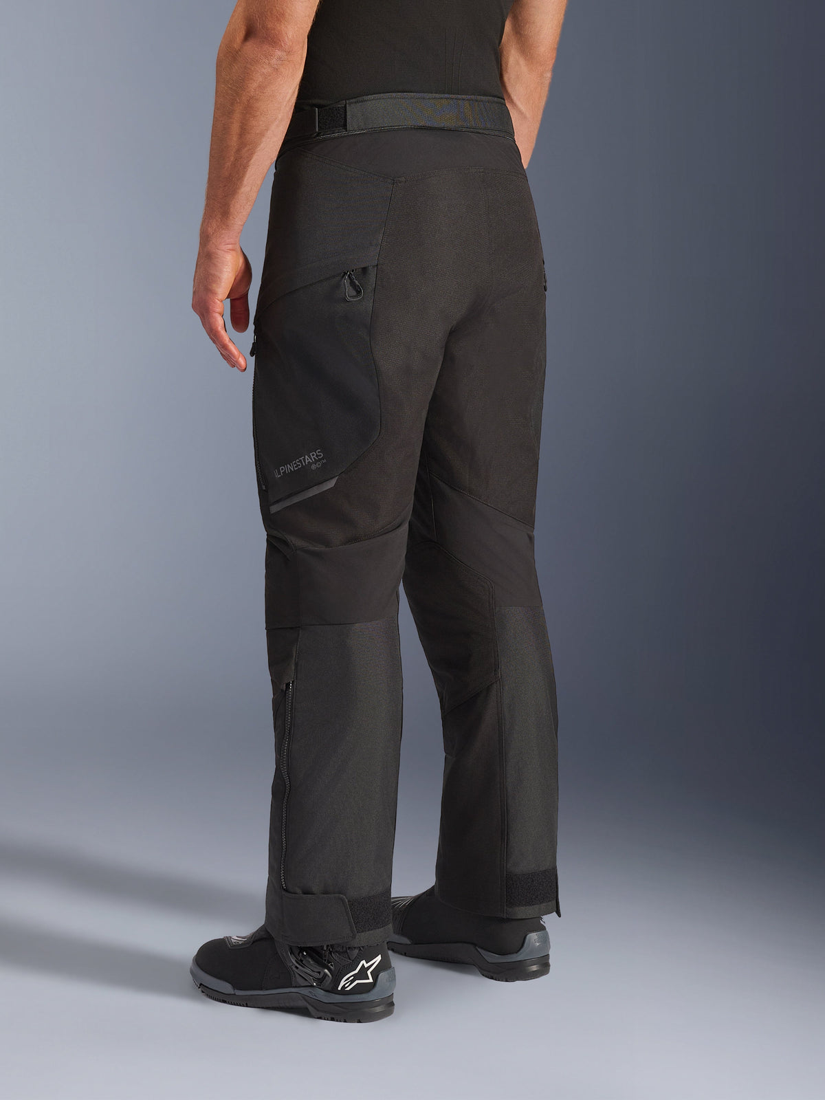 Alpinestars Cusco Drystar® Pants, Motorcycle Pants, Black, rear three-quarter view showing zippered thigh pocket and articulated panels, worn with black motorcycle boots, durable adventure touring design with subtle branding
