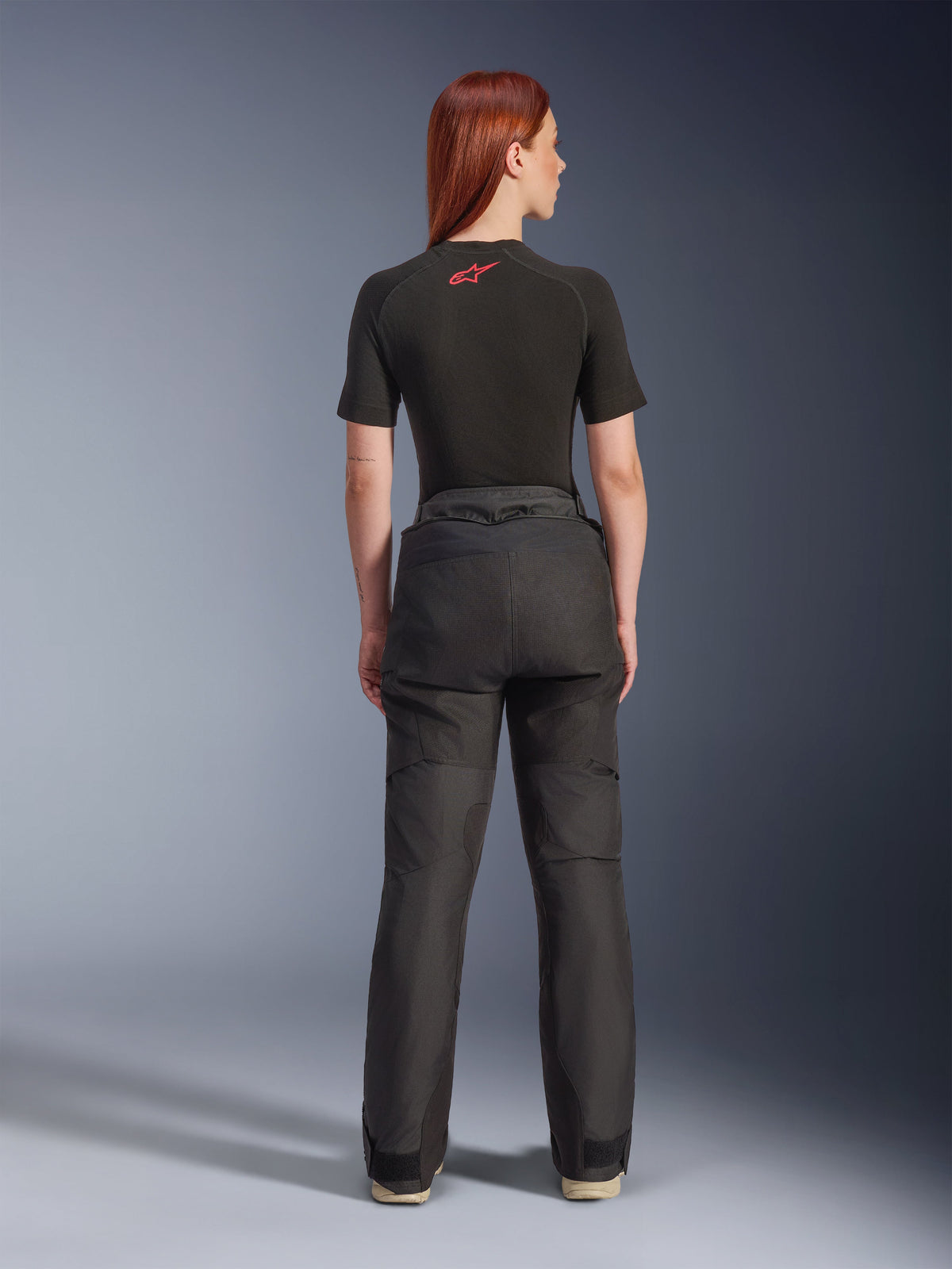 Vue arrière d'un mannequin portant le pantalon Alpinestars Stella Andes V4 Drystar® noir, associé à une sous-couche noire à manches courtes ornée d'un logo Alpinestars rouge, équipement de moto d'aventure-touring avec une construction textile durable.