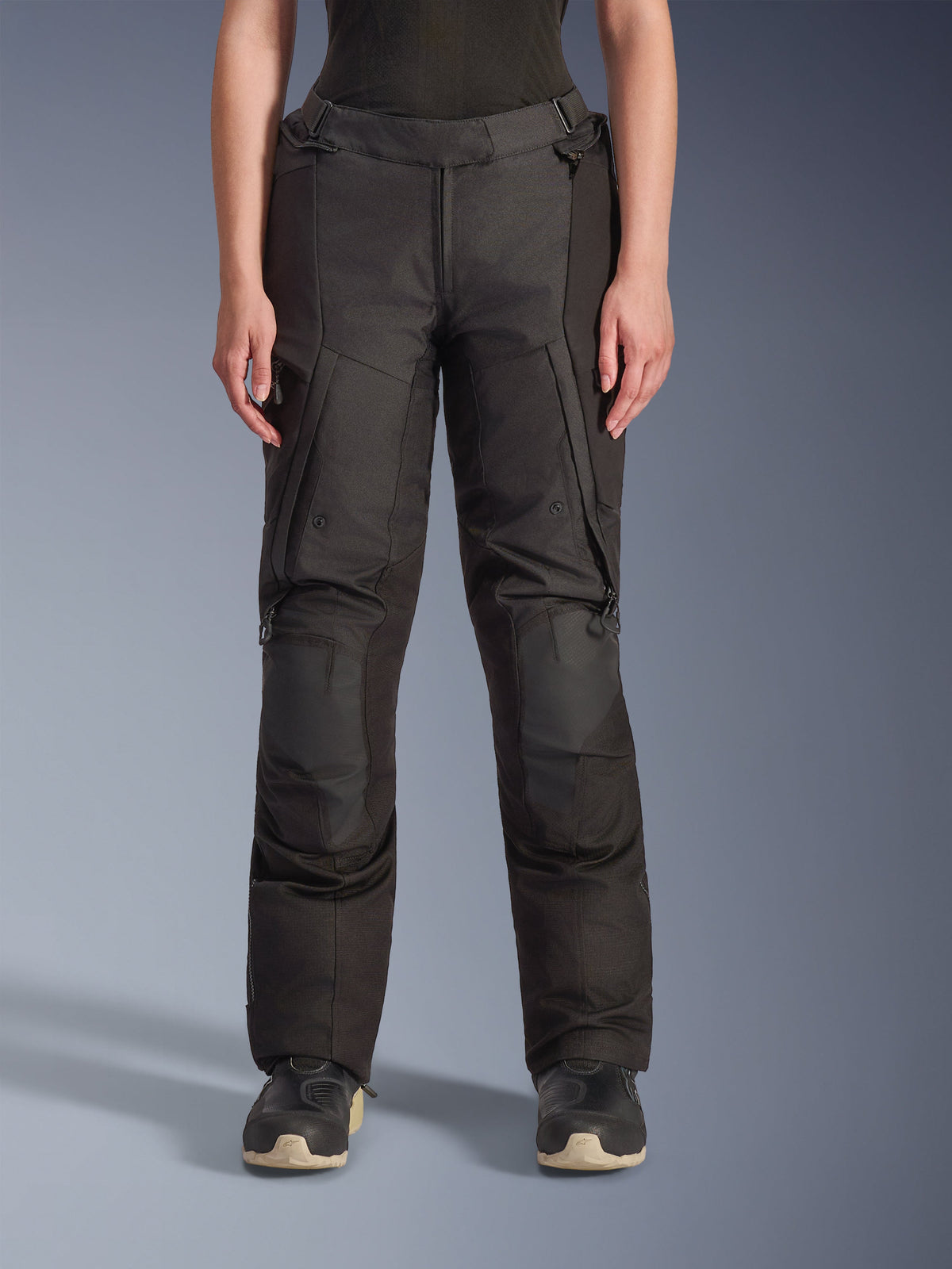 Alpinestars Stella Andes V4 Drystar, pantalon de moto d'aventure pour femme, noir, vue de face, doté de panneaux de genoux renforcés, de poches cargo résistantes à l'eau et de sangles de taille réglables, porté avec des bottes noires en studio.