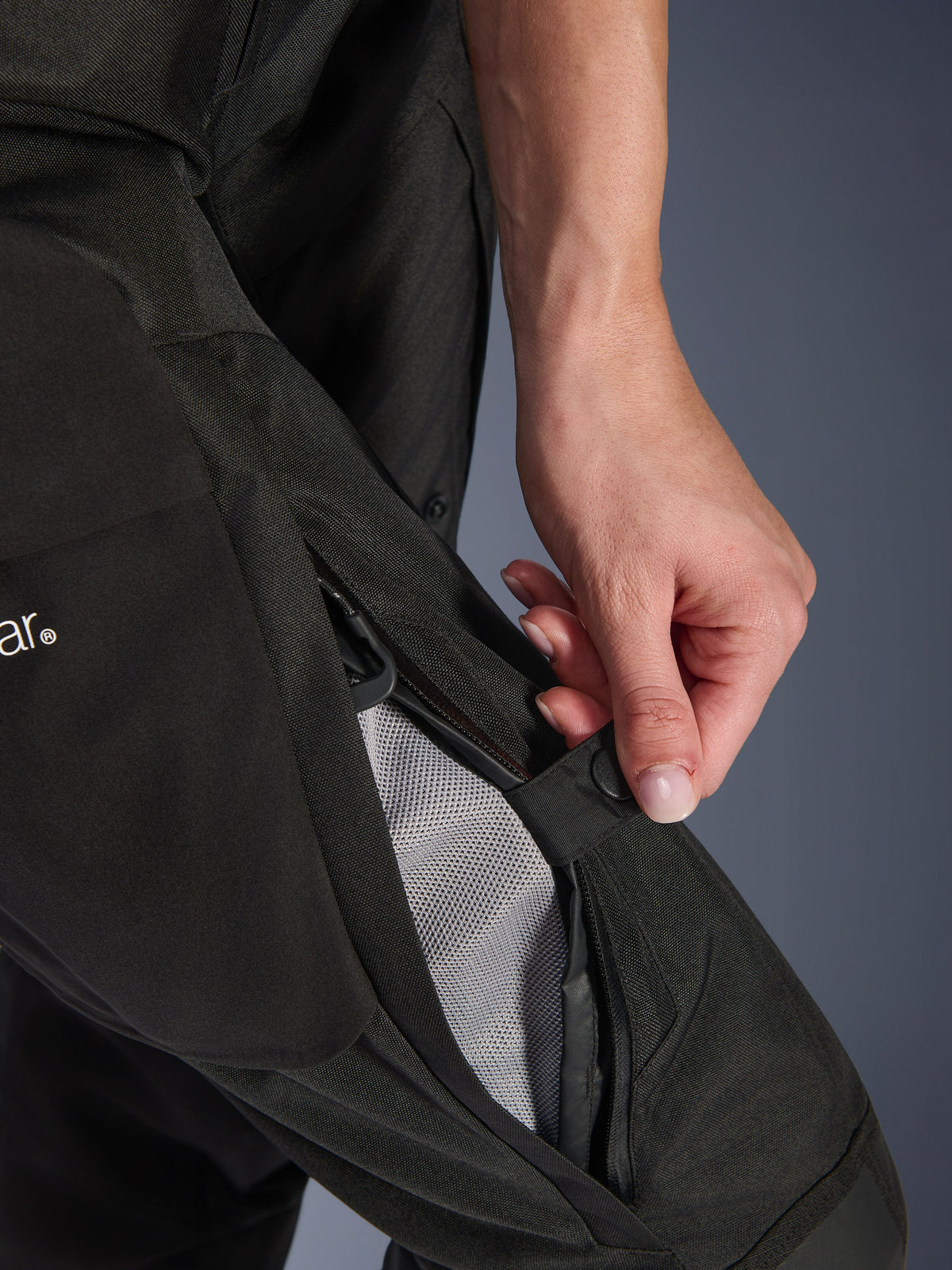 Pantalon femme Alpinestars Stella Andes V4 Drystar®, pantalon de moto, noir, gros plan d'une main ouvrant la ventilation zippée au niveau de la cuisse pour révéler la doublure en mesh favorisant la circulation de l'air, équipement d'aventure en textile durable