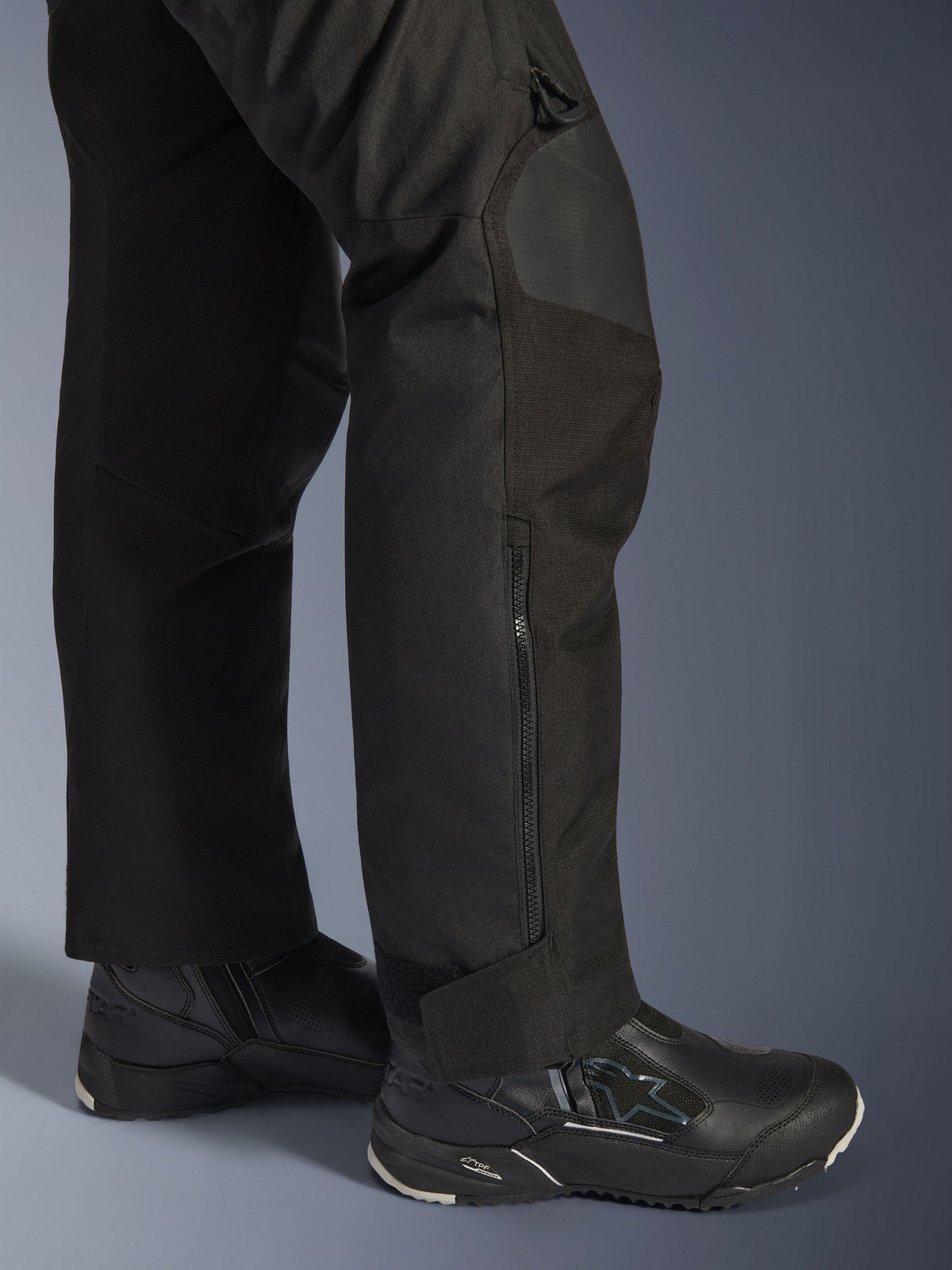 Pantalon Alpinestars Stella Andes V4 Drystar®, pantalon de moto pour femme, noir, gros plan sur le bas de la jambe avec fermeture éclair latérale et revers de cheville réglable, porté avec des bottes de moto Alpinestars noires