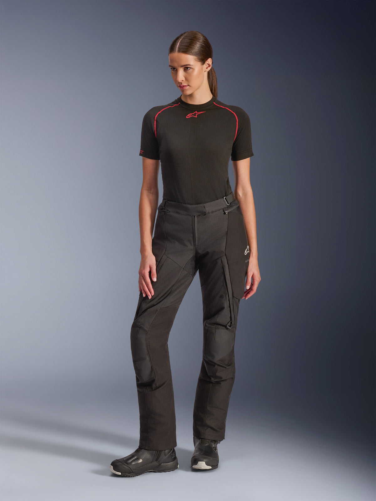 Pantalon Alpinestars Stella Andes V4 Drystar®, pantalon de moto d'aventure pour femme, noir, porté par un mannequin avec une couche de base noire à manches courtes et des bottes de moto noires, avec genoux renforcés et poches cargo, conception ergonomique pour le touring par tous les temps.