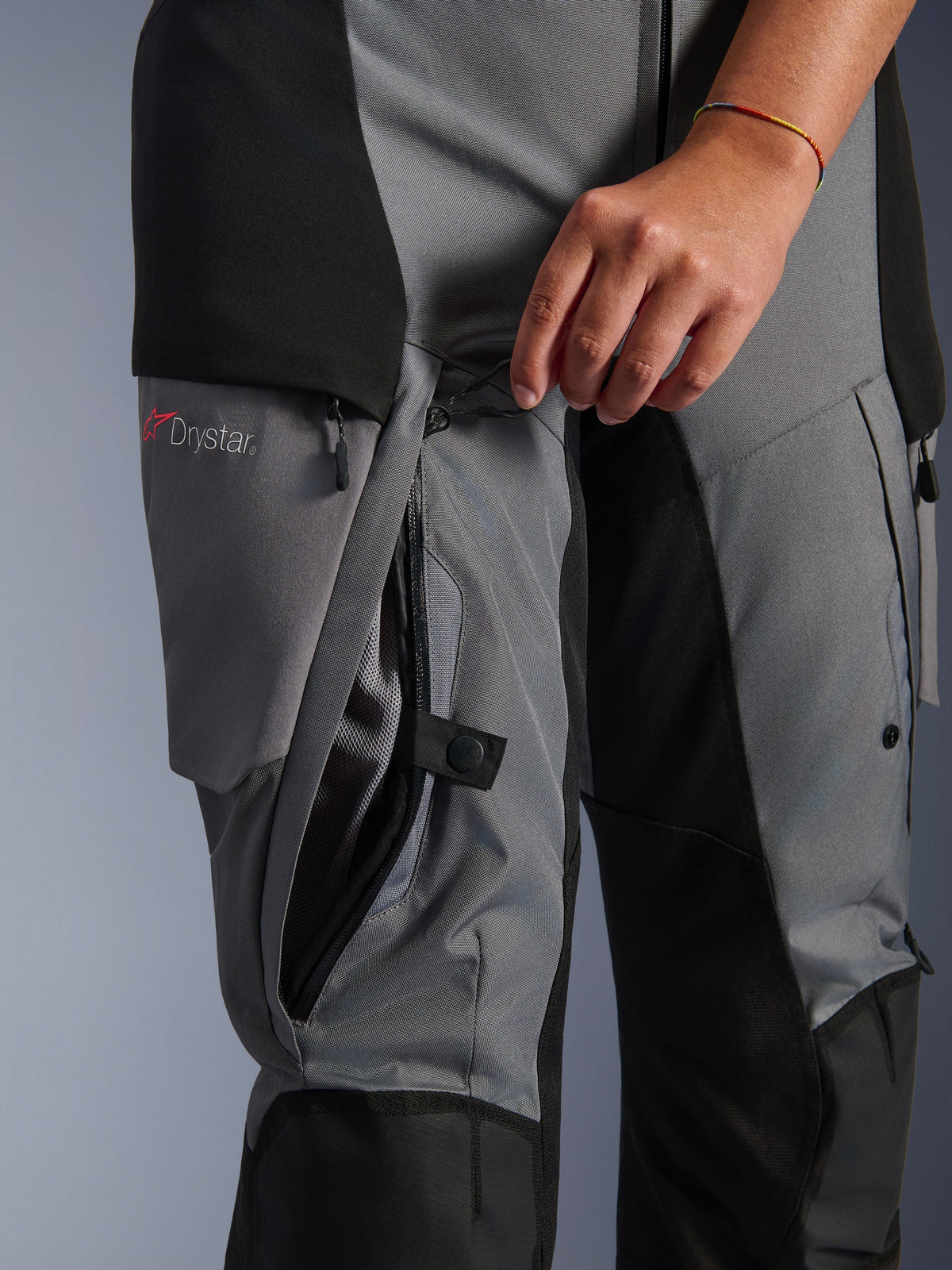 Pantalon Alpinestars Stella Andes V4 Drystar, textile noir et gris foncé, gros plan d'une fermeture éclair de ventilation sur la cuisse ouverte à la main, doublure en mesh visible, logo Drystar, équipement de moto d'aventure
