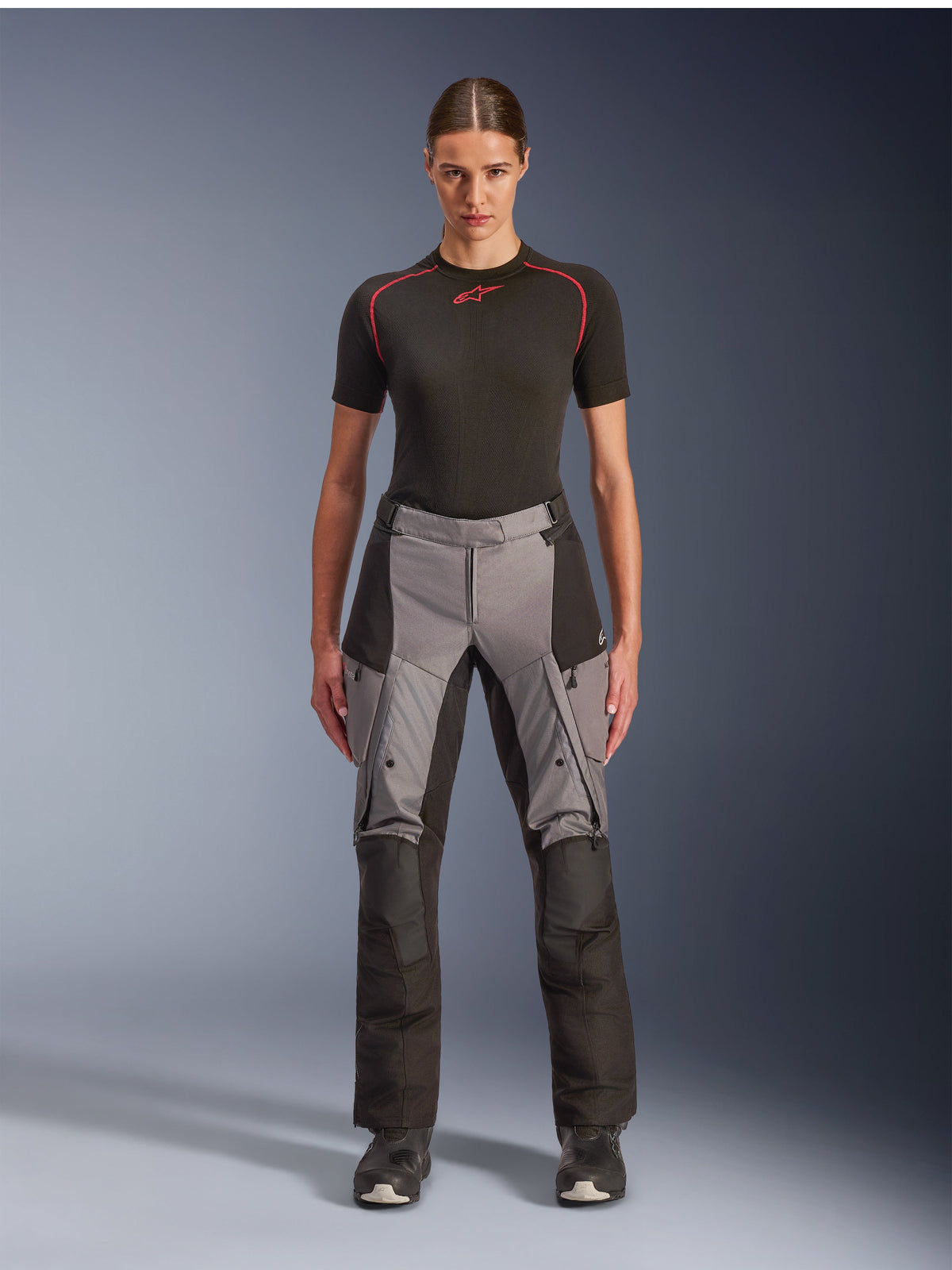 Alpinestars Stella Andes V4 Drystar Pants, pantalon de moto adventure touring pour femme, noir et gris foncé, porté par un mannequin femme avec une couche de base noire et des bottes de moto, doté de panneaux textiles renforcés et de poches cargo pour la conduite aventure