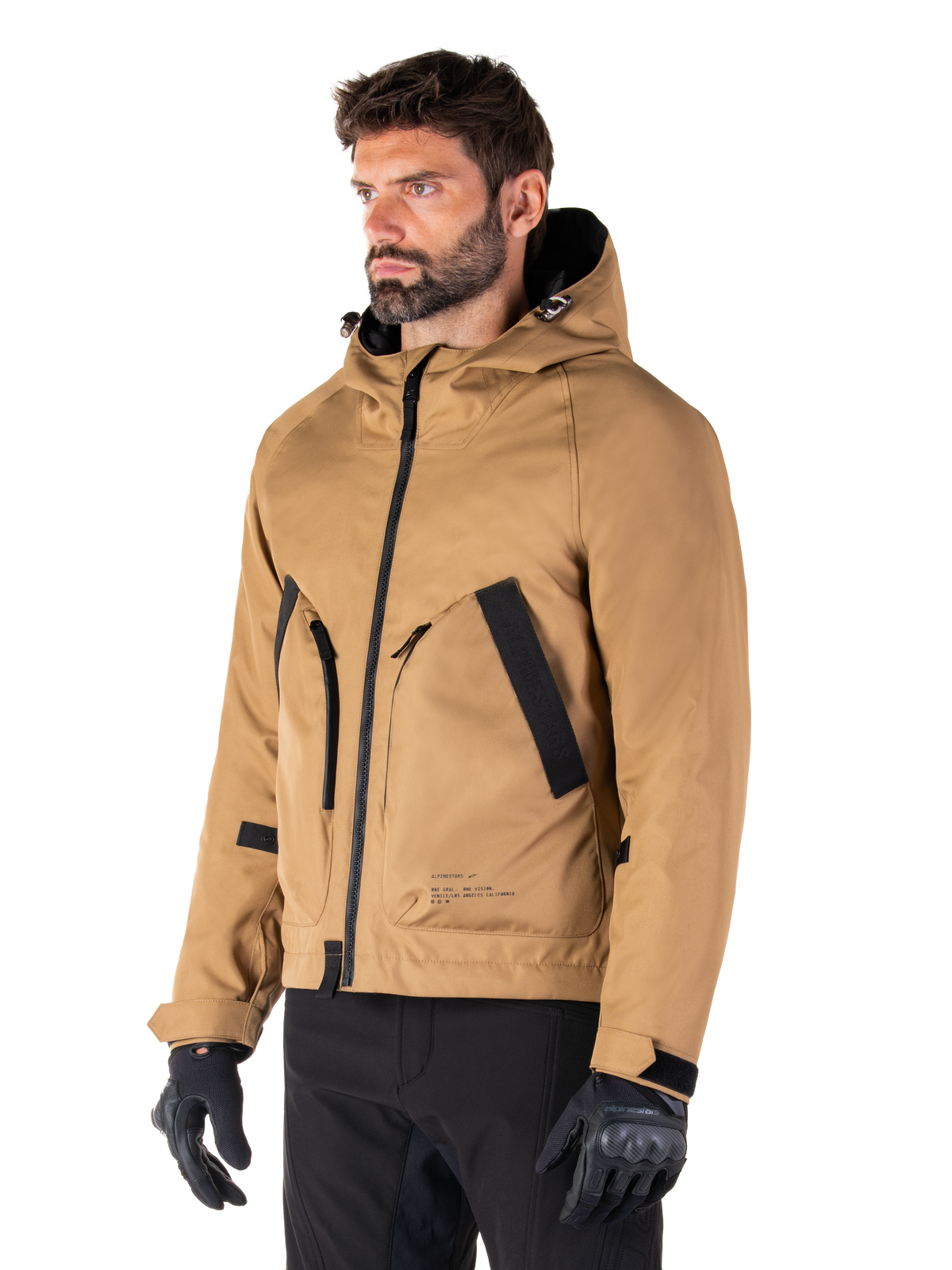 Parka imperméable Alpinestars Morush, Brun, mannequin masculin portant la parka avec des gants de moto noirs et un pantalon noir, design minimaliste d'inspiration streetwear doté d'une capuche anti-tempête et de grandes poches avant, équipement de moto imperméable