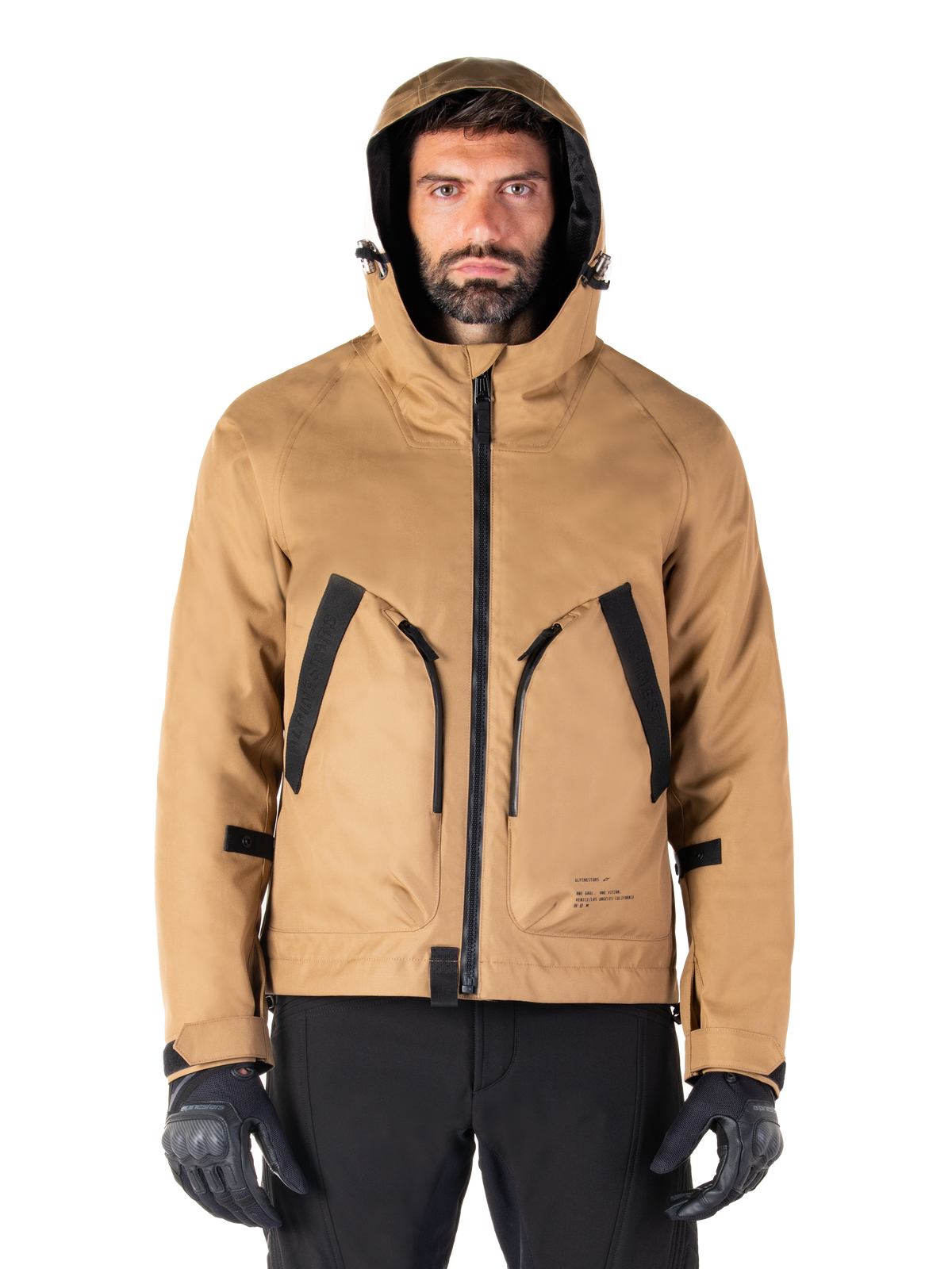 Alpinestars Morush Waterproof Parka, veste de moto, brun utility, design à capuche inspiré du streetwear avec de grandes poches avant aux accents noirs, portée avec des gants et un pantalon de moto noirs, équipement de moto urbain contemporain