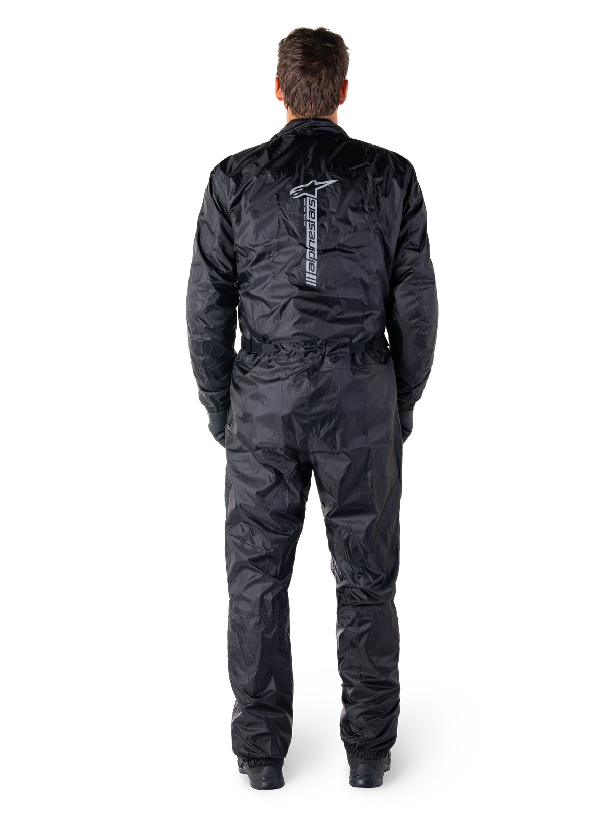Combinaison Alpinestars Hurricane Rain V2, combinaison de moto imperméable une pièce noire, vue arrière montrant le grand mot-symbole et logo Alpinestars verticaux, tissu froissé léger avec taille et poignets élastiqués, conçue pour la protection lors de la conduite par temps humide.