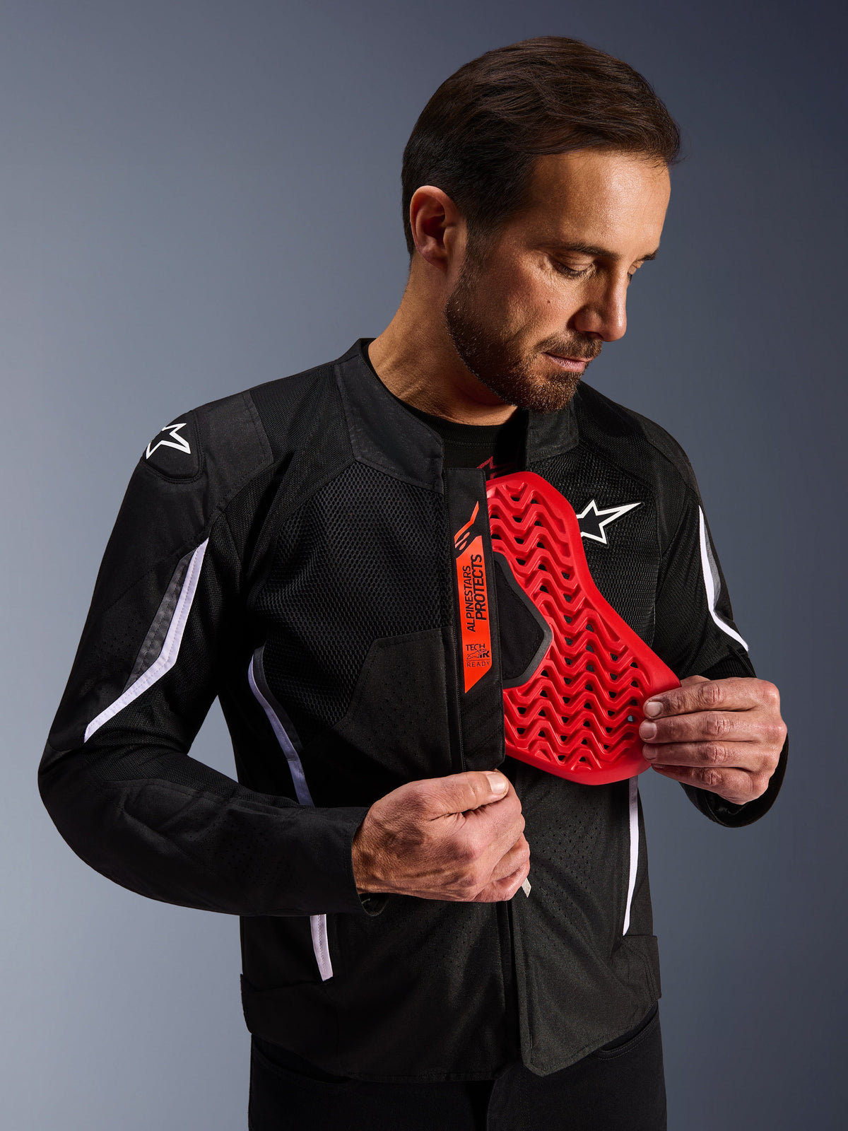 Veste Alpinestars AST V3 Air en noir, homme dévoilant un insert de protection de poitrine rouge vif au motif nid d'abeille, mettant en avant la compatibilité Tech-Air Ready et la protection interne intégrée pour la sécurité à moto.
