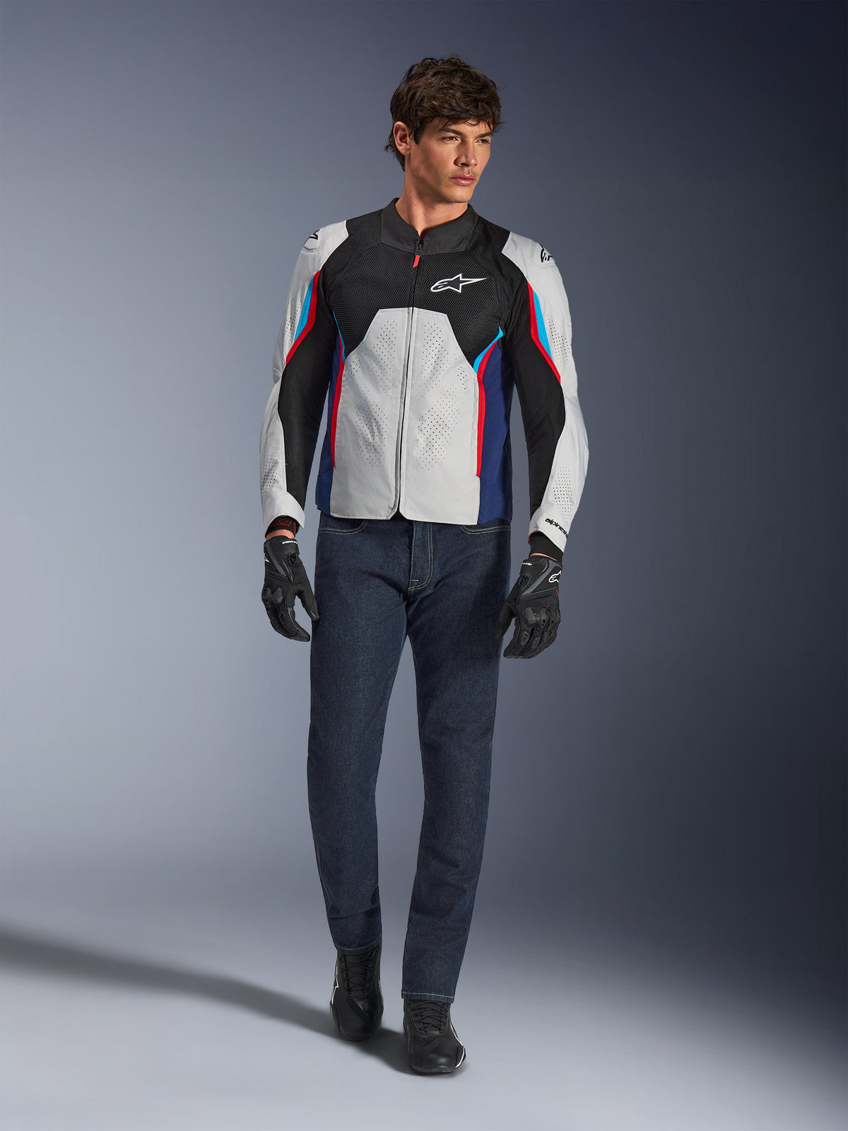 Mannequin homme portant la veste Alpinestars AST V3 Air en Silver Deep Blue Bright Red, dotée d'une ventilation en maille et de panneaux perforés, associée à un jean de moto en denim foncé et des gants noirs, équipement de moto sportif pour temps chaud.