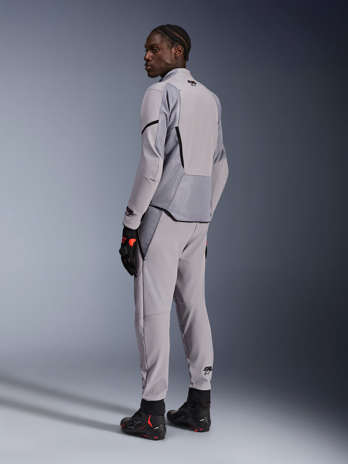 Veste Alpinestars Aeroshell Airflow en Mid Gray Anthracite, portée avec un pantalon assorti et des gants de course noirs, vue de dos montrant les panneaux perforés au laser et la coupe sport athlétique, équipement de moto professionnel
