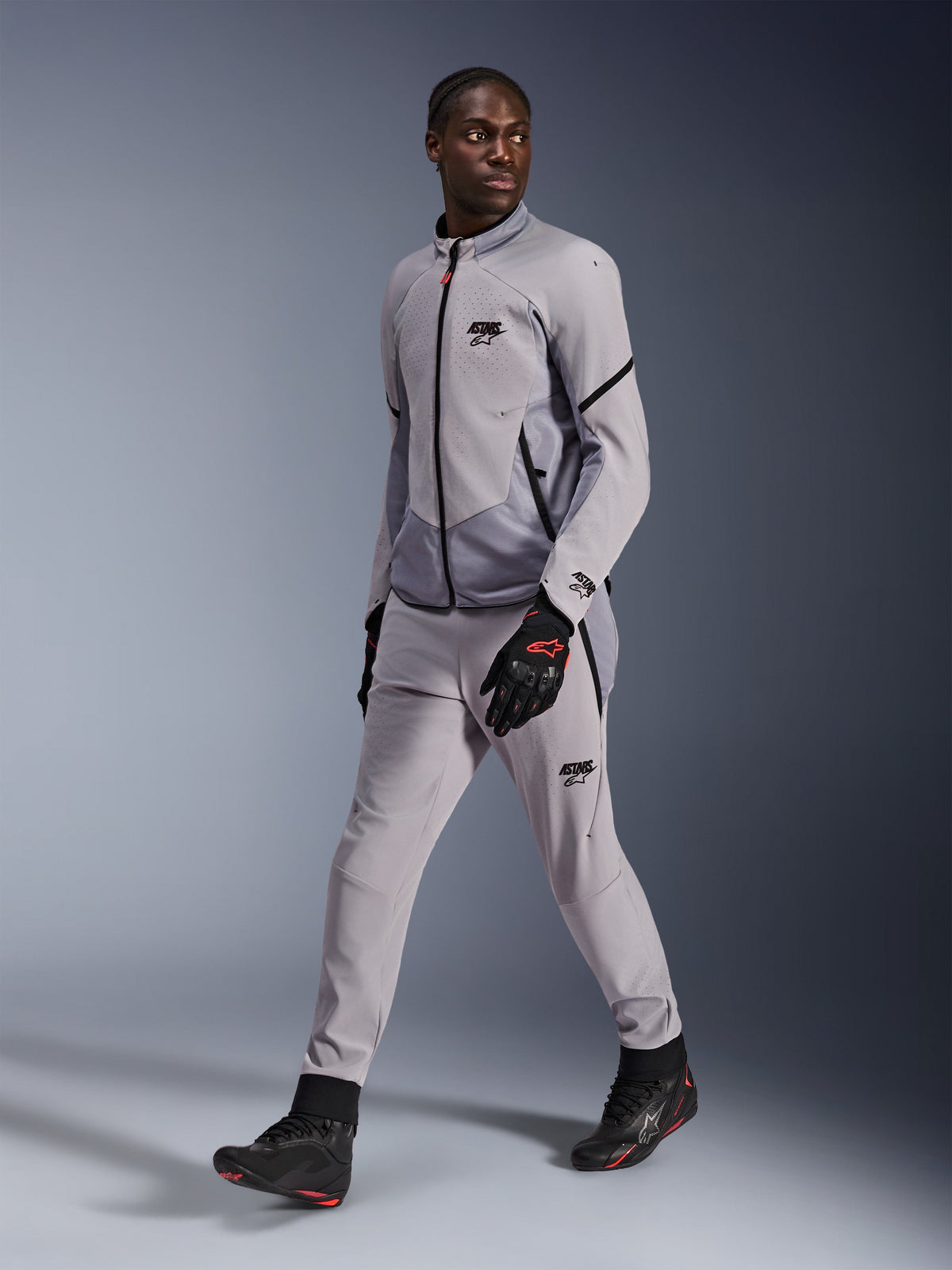 Veste Alpinestars Aeroshell Airflow en Gris Moyen Anthracite, portée par un mannequin homme avec un pantalon de moto gris assorti et des gants noirs, dotée d'une ventilation de poitrine perforée au laser et d'un design à coupe sportive.