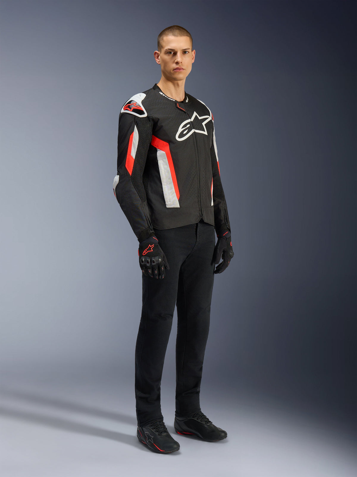 Veste Alpinestars T-GP Air, Noir Rouge Fluo, portée par un mannequin avec un pantalon de moto et des gants noirs, dotée de panneaux textiles perforés au laser, logos Alpinestars blancs et accents rouges, veste de moto sportive pour la conduite sur route par temps chaud