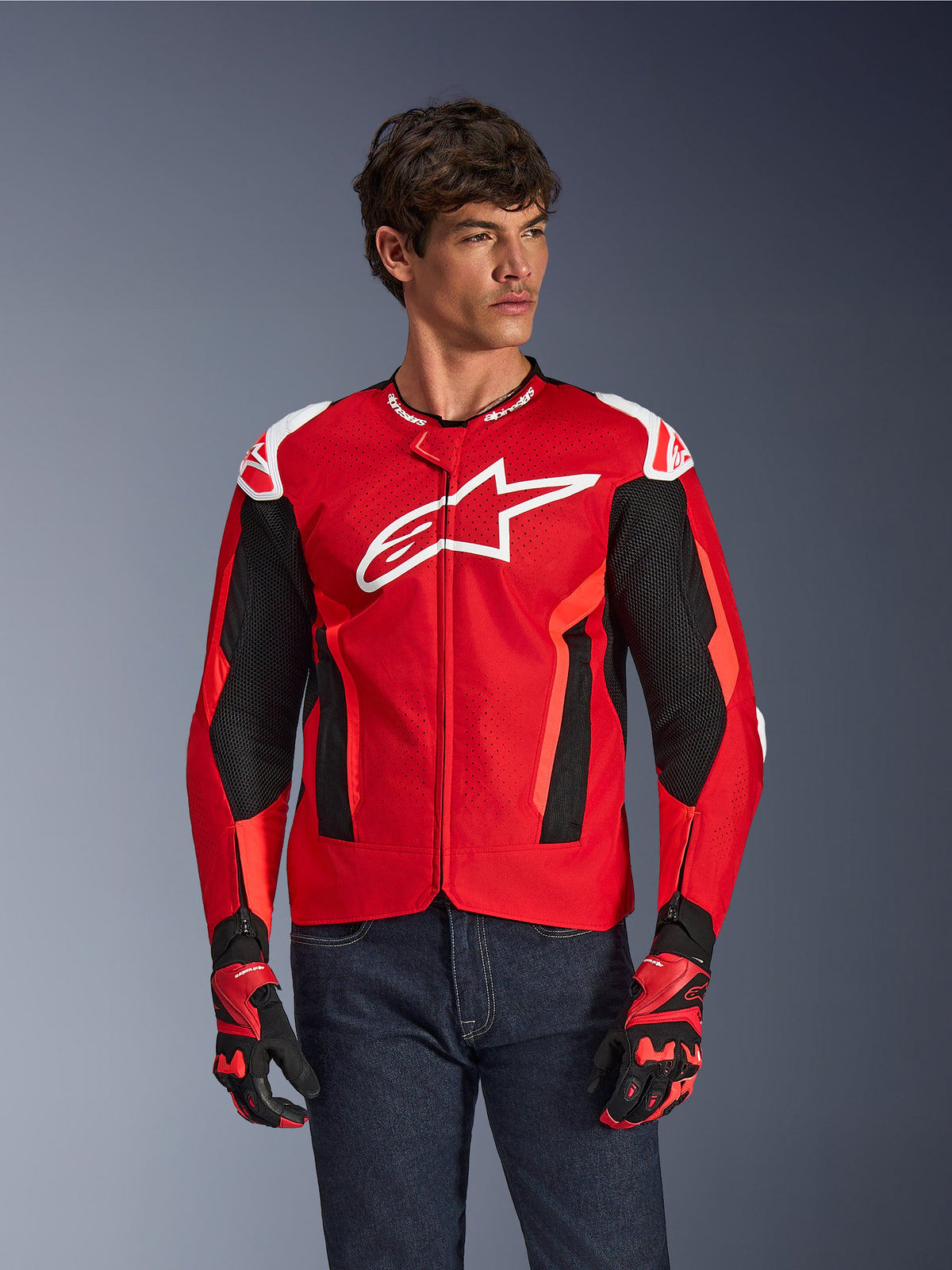 Alpinestars T-GP Air Jacket, veste de moto, rouge vif et noir avec logo blanc, dotée de panneaux de ventilation en maille perforée, portée avec des gants assortis et un jean en denim foncé, design sportif pour la conduite par temps chaud