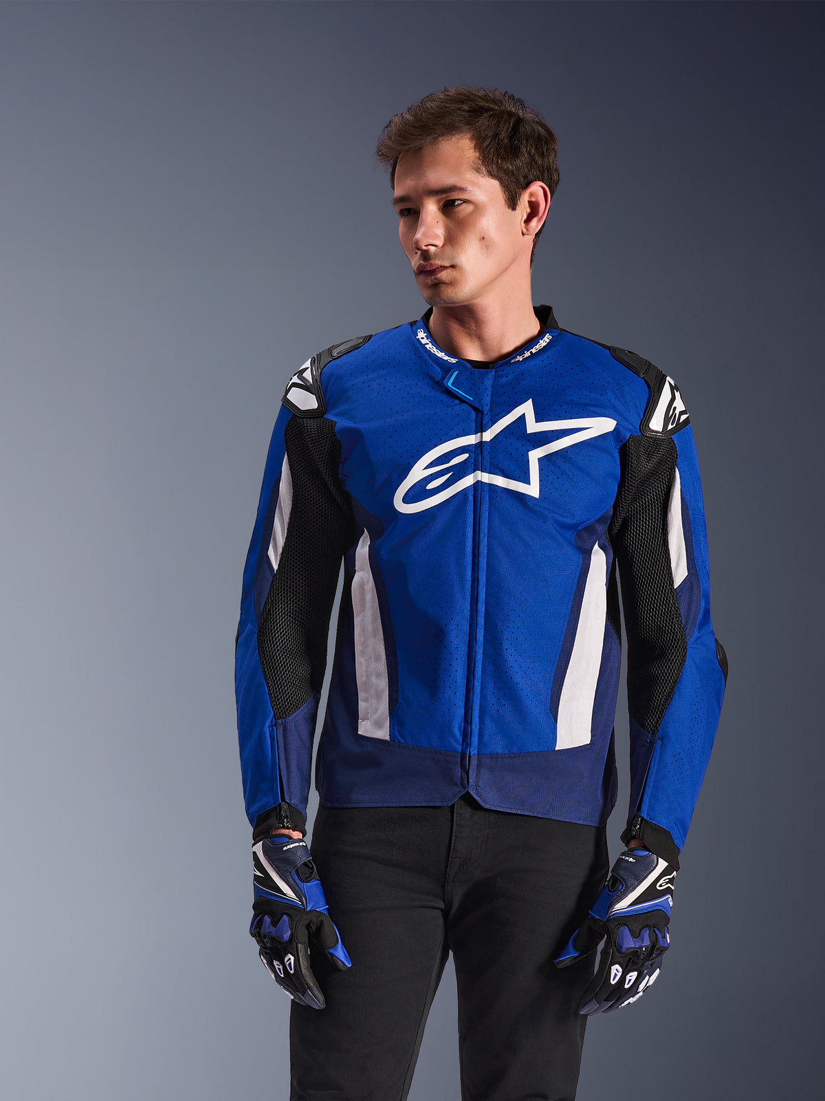 Alpinestars T-GP Air Jacket, veste de moto textile sport, bleu vif et bleu marine avec des accents blancs, arborant un grand logo étoile sur la poitrine, panneaux de ventilation en mesh, portée par un mannequin avec des gants assortis et un pantalon noir