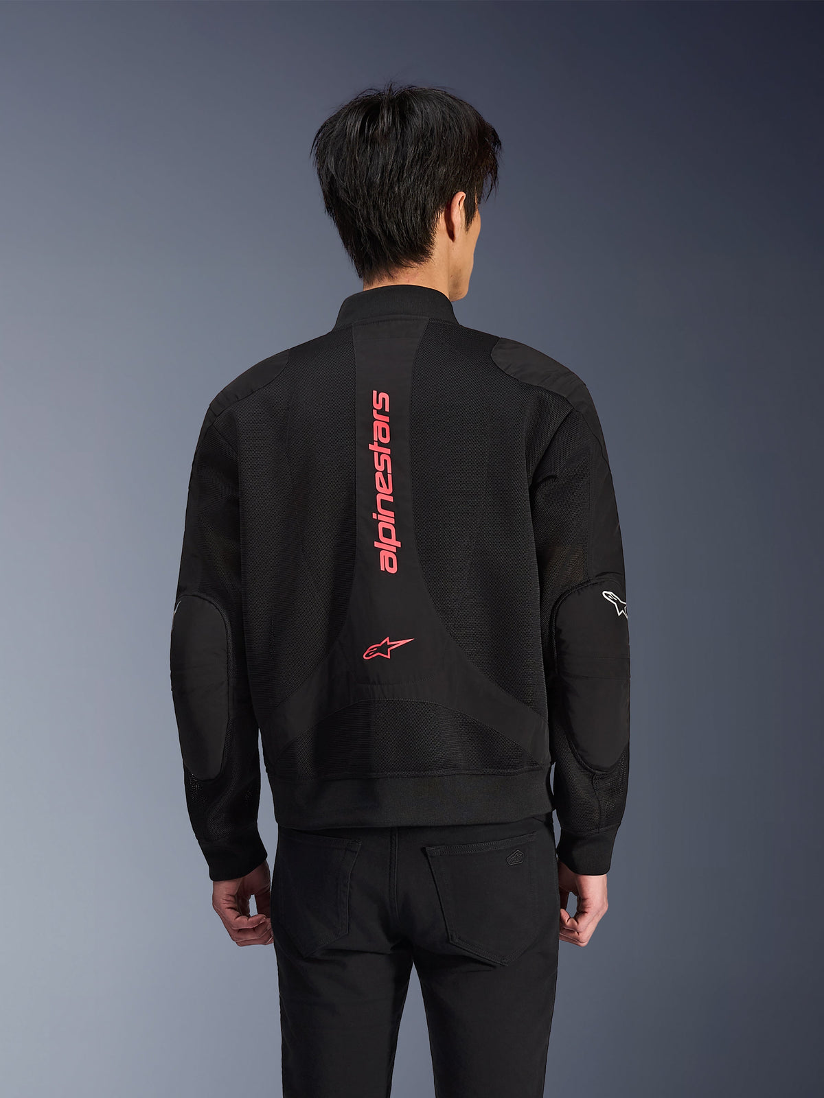 Rear view of a rider wearing the Alpinestars Flight Air Jacket in Black Bright Red, urban bomber-style motorcycle jacket with 3D mesh construction, featuring large vertical red Alpinestars branding and star logo on the back, street-inspired technical gear