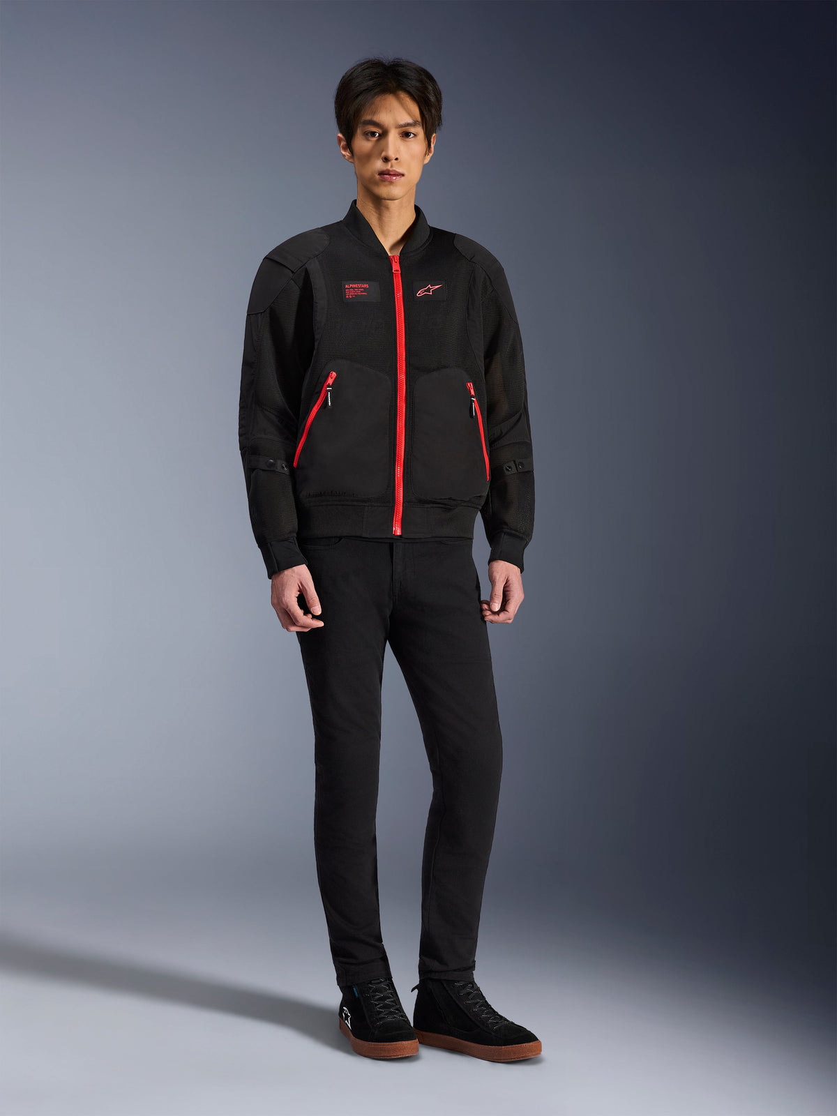 Alpinestars Flight Air Jacket in Black Bright Red, bomber-style urban motorcycle jacket featuring 3D mesh panels and vibrant red zippers, worn by a model with black slim-fit pants and black sneakers, street-inspired contemporary riding gear