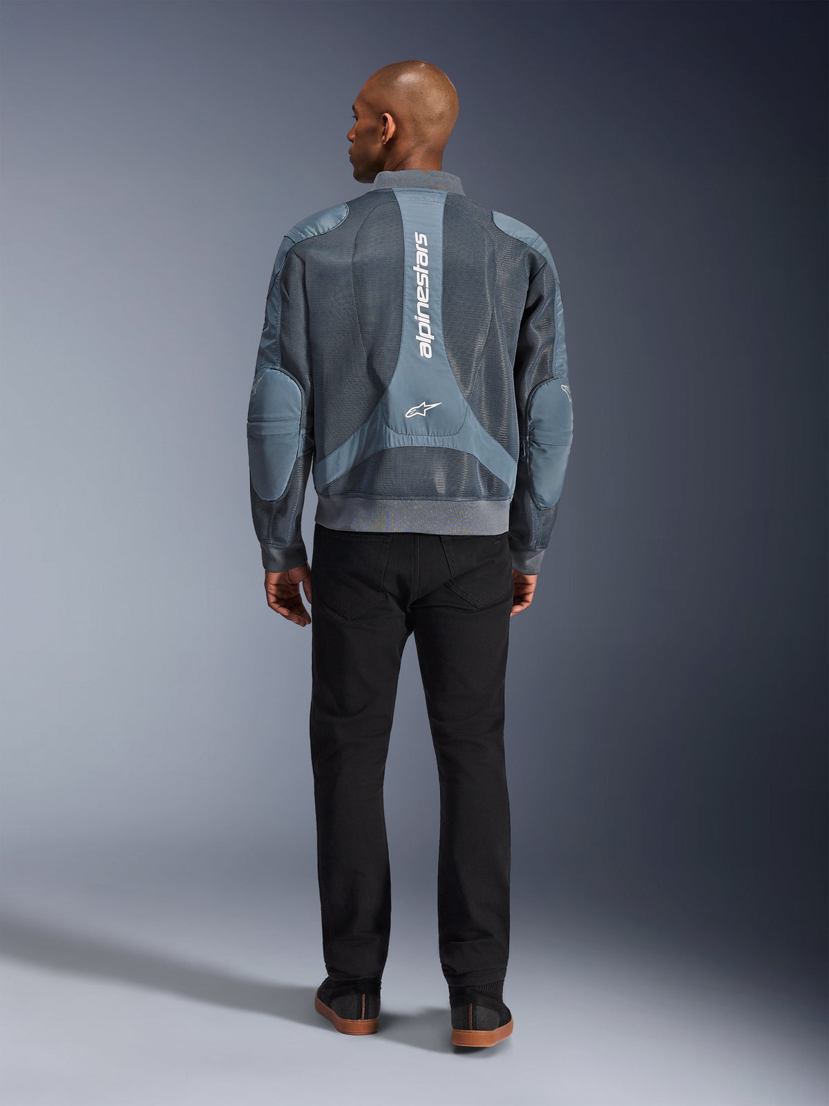 Veste Alpinestars Flight Air en Storm Gray, vue de dos d'un mannequin homme portant une veste de moto au style urbain avec panneaux en maille 3D et logo Alpinestars vertical, associée à un pantalon noir pour un look urbain moderne