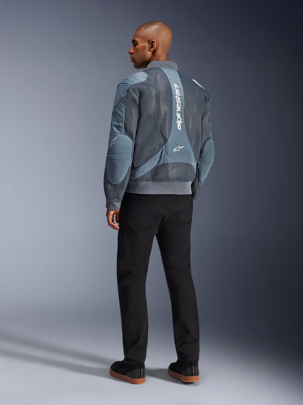 Veste Alpinestars Flight Air, veste de moto Storm Gray, vue de dos, avec panneaux de ventilation en maille 3D et marquage Alpinestars vertical blanc, portée avec un pantalon noir et des baskets noires, style urbain