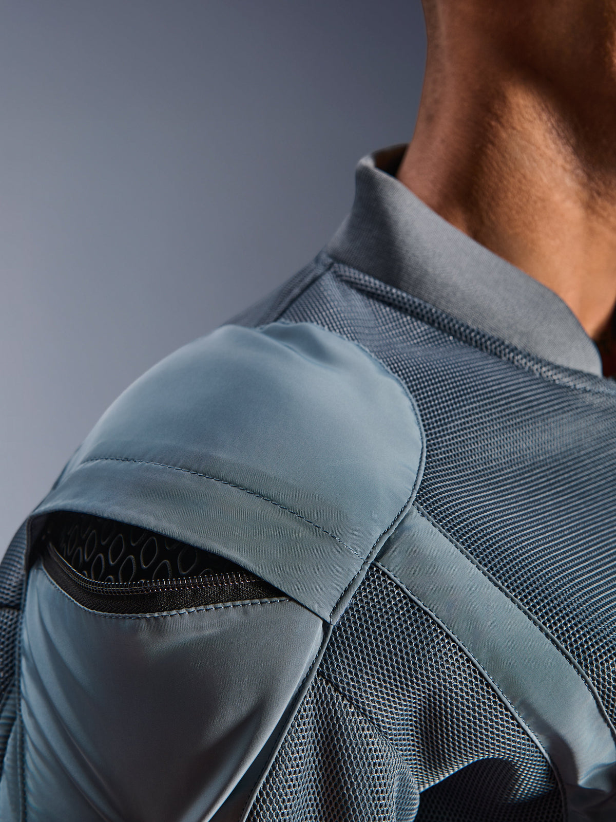 Gros plan sur la veste Alpinestars Flight Air en Storm Gray, mettant en évidence la poche de protection d'épaule externe avec armure en nid d'abeille visible, les panneaux de ventilation en maille 3D et le col côtelé pour la conduite moto urbaine technique