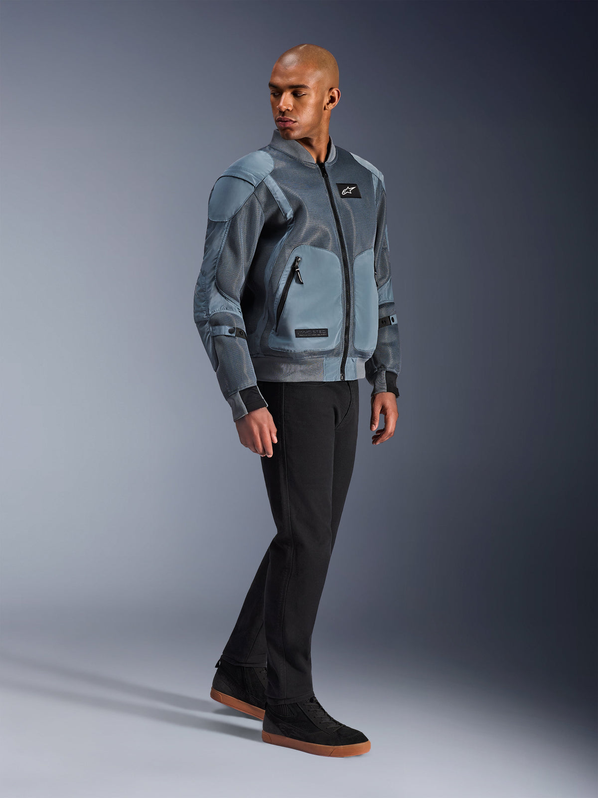 Veste Alpinestars Flight Air, Storm Gray, veste de moto urbaine d'inspiration bomber, portée par un mannequin homme avec pantalon noir et baskets, dotée de panneaux de ventilation étendus en maille 3D et de poches de protection externes, équipement de protection streetwear moderne pour la conduite par temps chaud