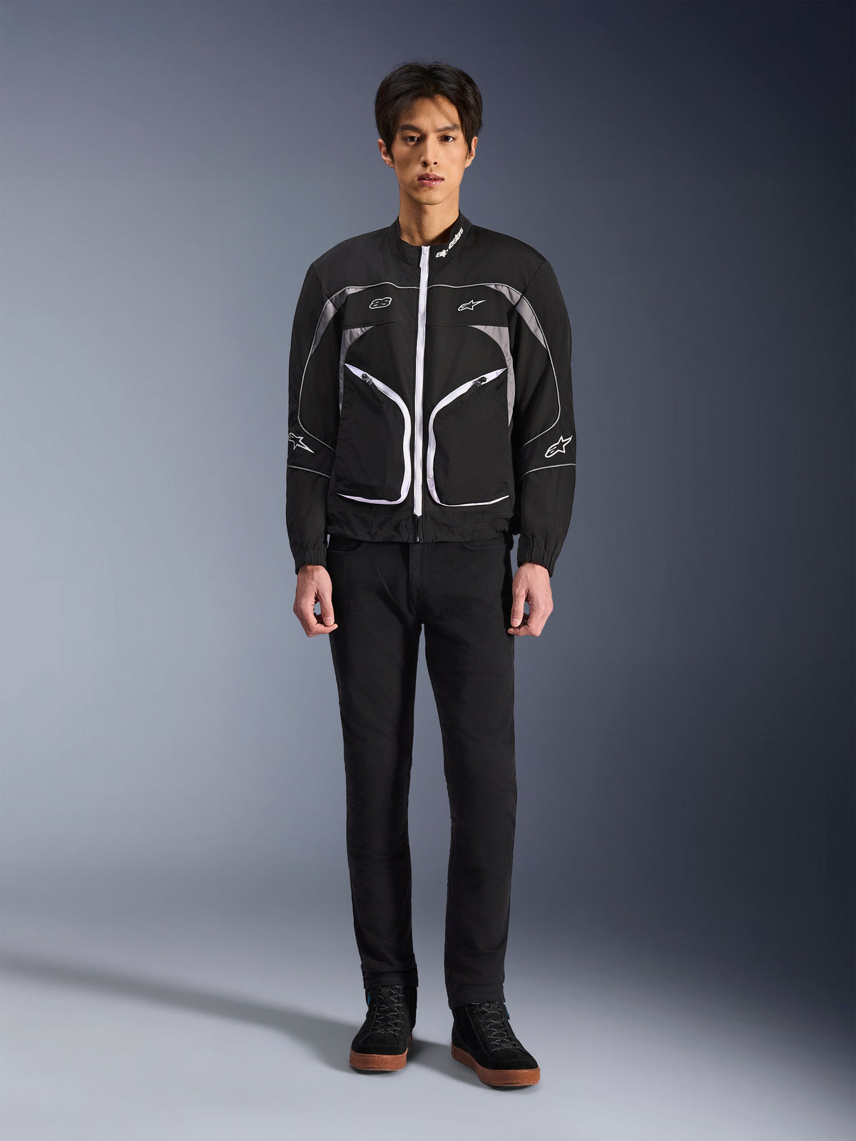 Alpinestars Unite Jacket, Motorcycle Jacket, Black and Dark Gray, worn by a model with black pants and black boots, featuring white contrast zippers, reflective piping, and minimalist urban design