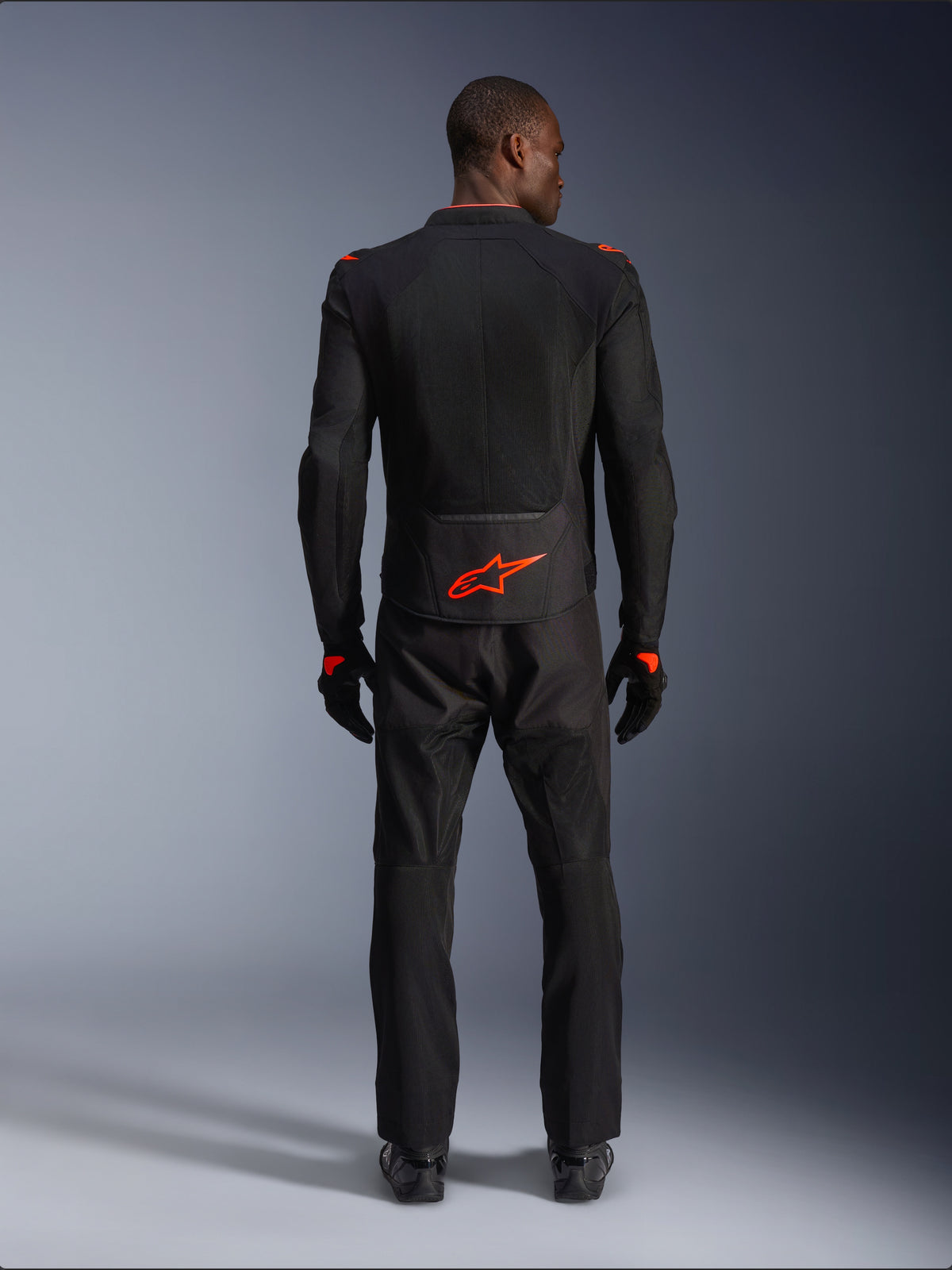 Veste Alpinestars Viper Air V4, noir et rouge fluo, vue de dos sur mannequin, portée avec un pantalon et des gants de moto assortis, logo rouge fluorescent vif au bas du dos, construction en mesh pour la circulation de l'air, coupe athlétique pour la conduite sur route