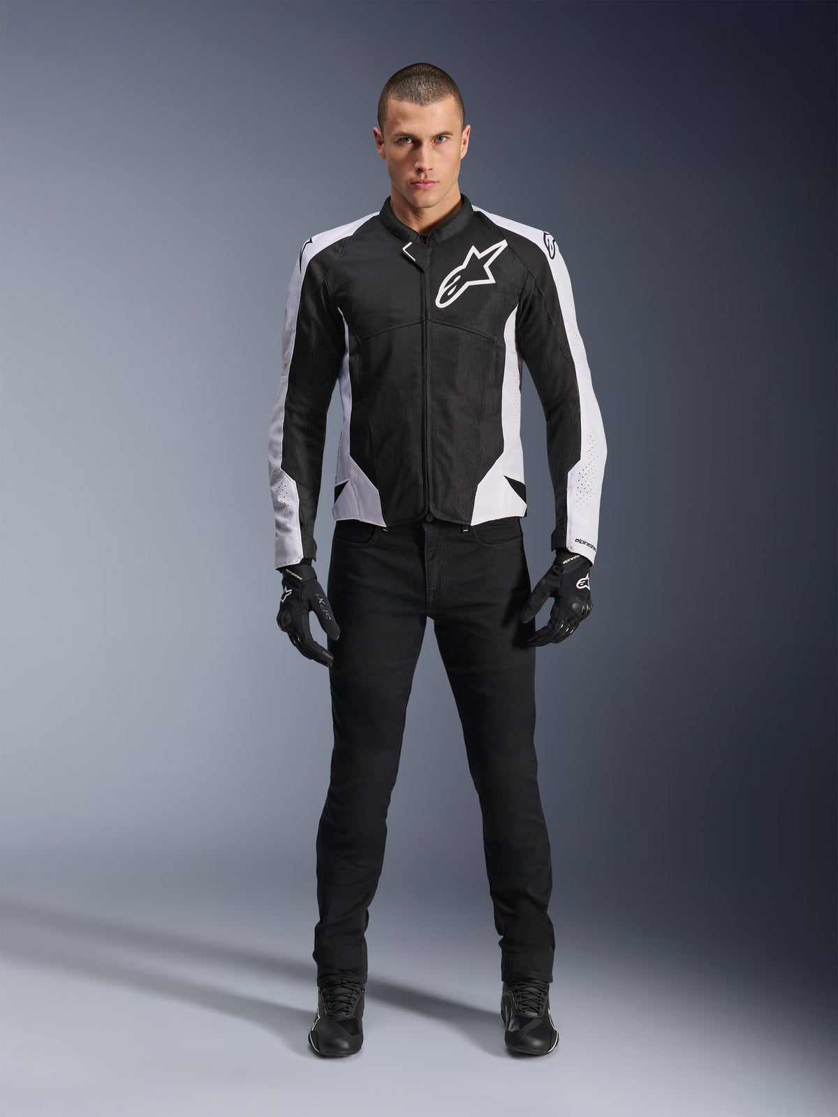 Veste Alpinestars Viper Air V4, veste de moto noire et blanche avec un grand logo blanc sur la poitrine, portée par un mannequin homme avec un pantalon noir et des gants, dotée de panneaux en maille pour la ventilation, vêtement de route sportif