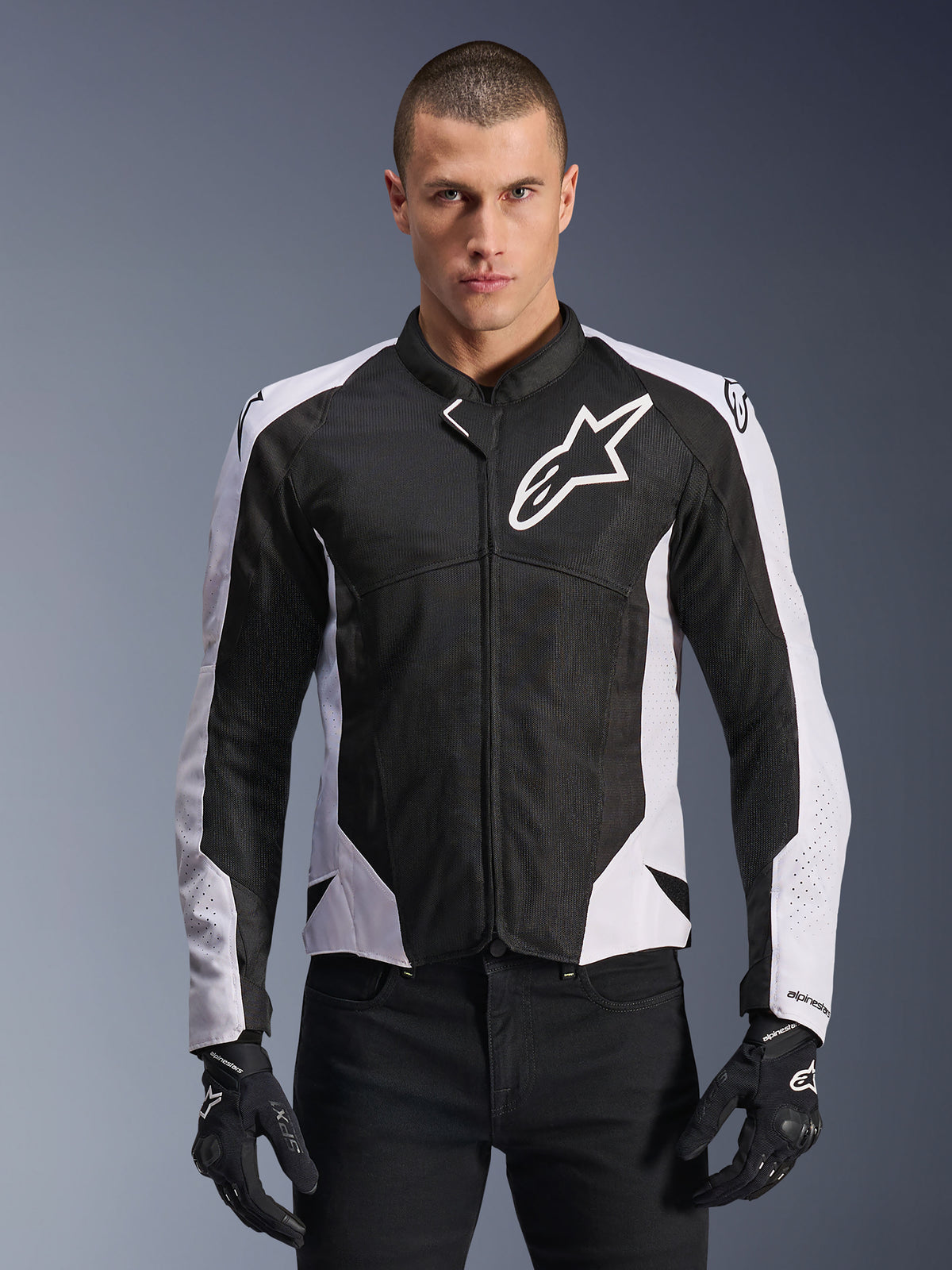 Veste Alpinestars Viper Air V4, veste de moto de course, noire et blanche, portée par un pilote, construction en maille technique et textile avec panneaux blancs aux épaules, logo étoile proéminent sur la poitrine, design sport haute performance, assortie à des gants de moto noirs