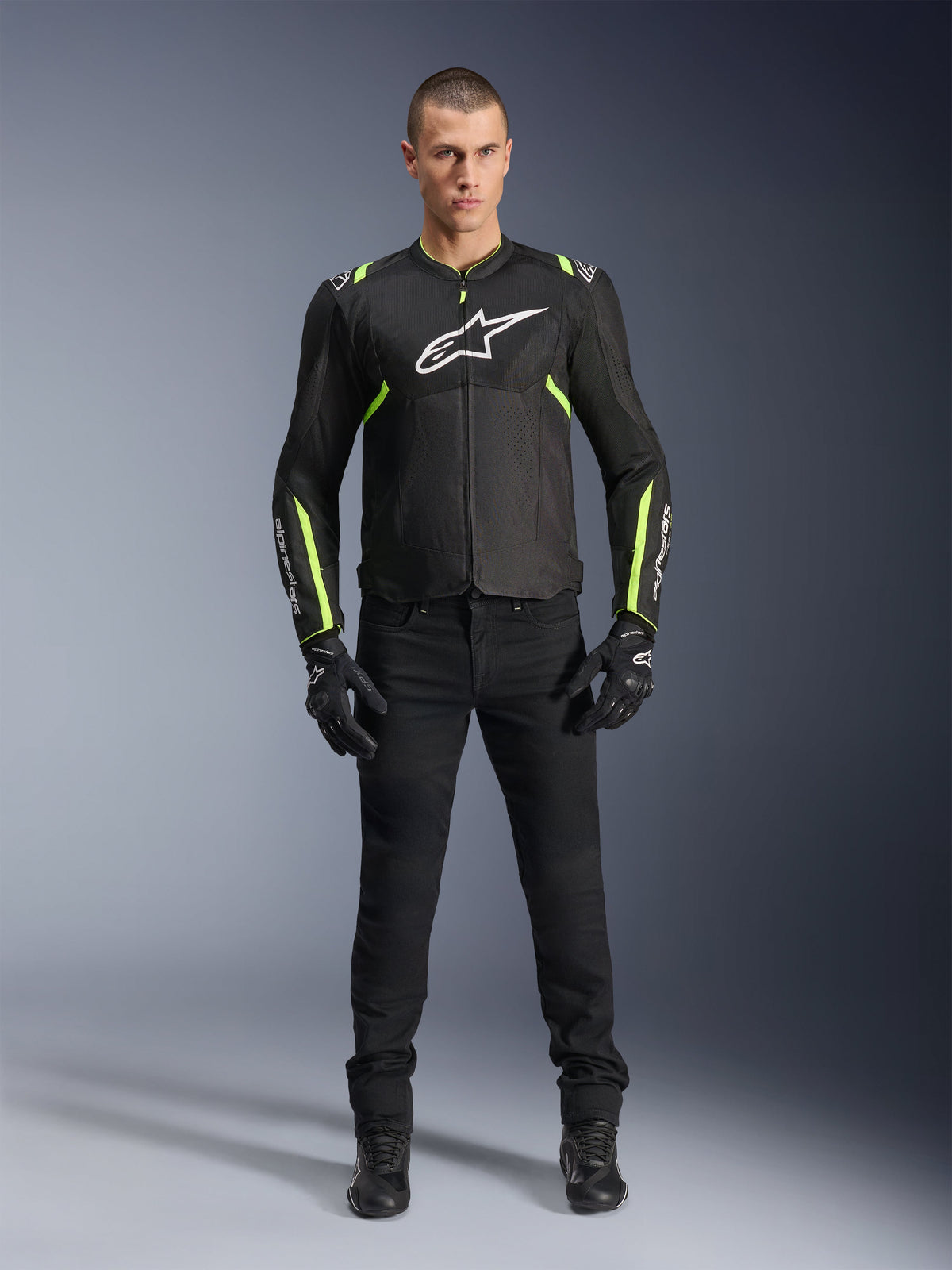 Veste Alpinestars T-Sps Air V2, noir et jaune fluo, veste de moto en textile avec panneaux en mesh, portée par un mannequin homme avec pantalon et gants noirs, arborant le logo Alpinestars blanc sur la poitrine, équipement de conduite sport urbain