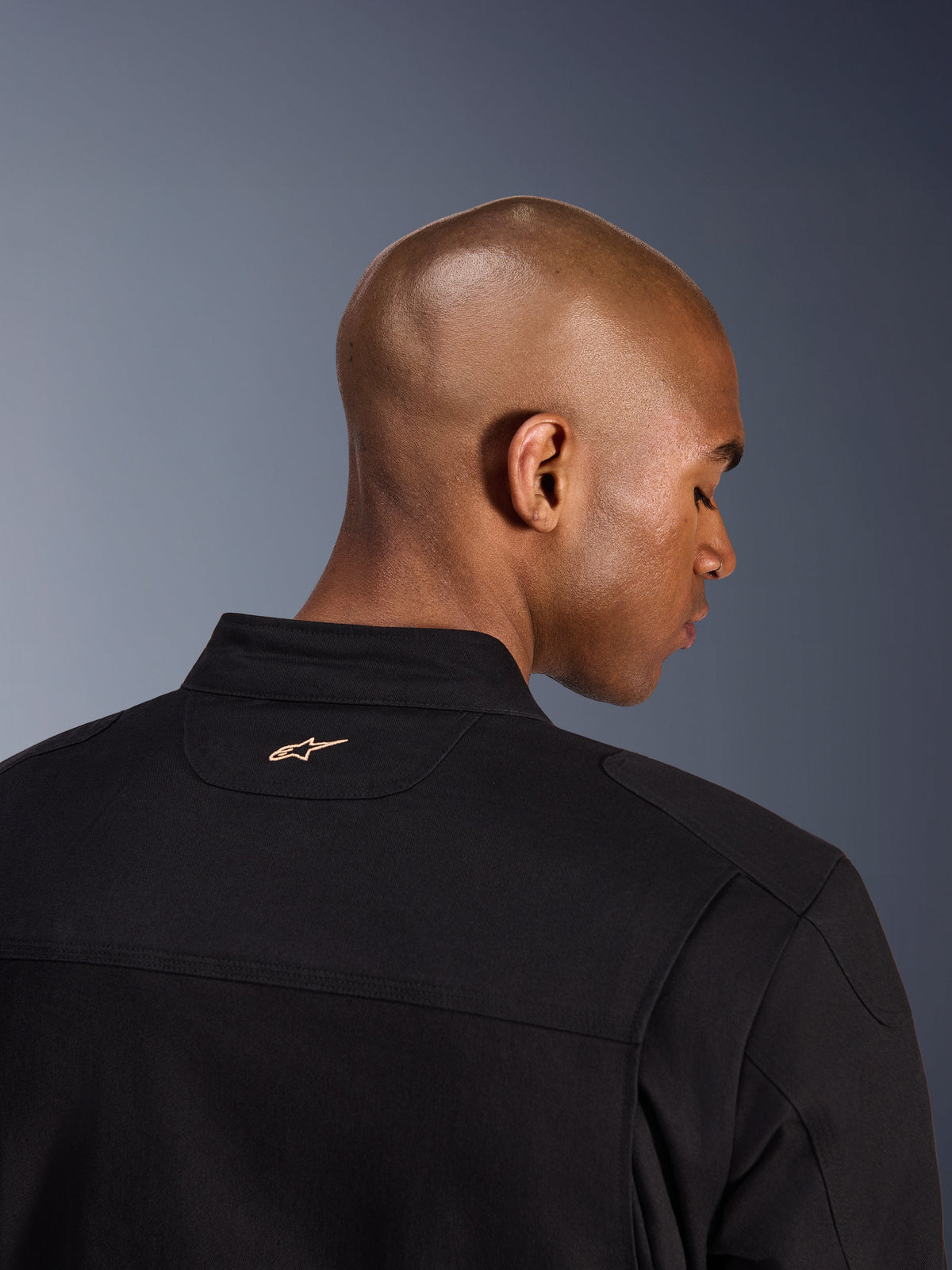 Alpinestars Bruiser Jacket, Black, back detail shot of the collar and upper shoulders, featuring a small tan embroidered Alpinestars logo on the neck, urban motorcycle jacket with workwear aesthetic