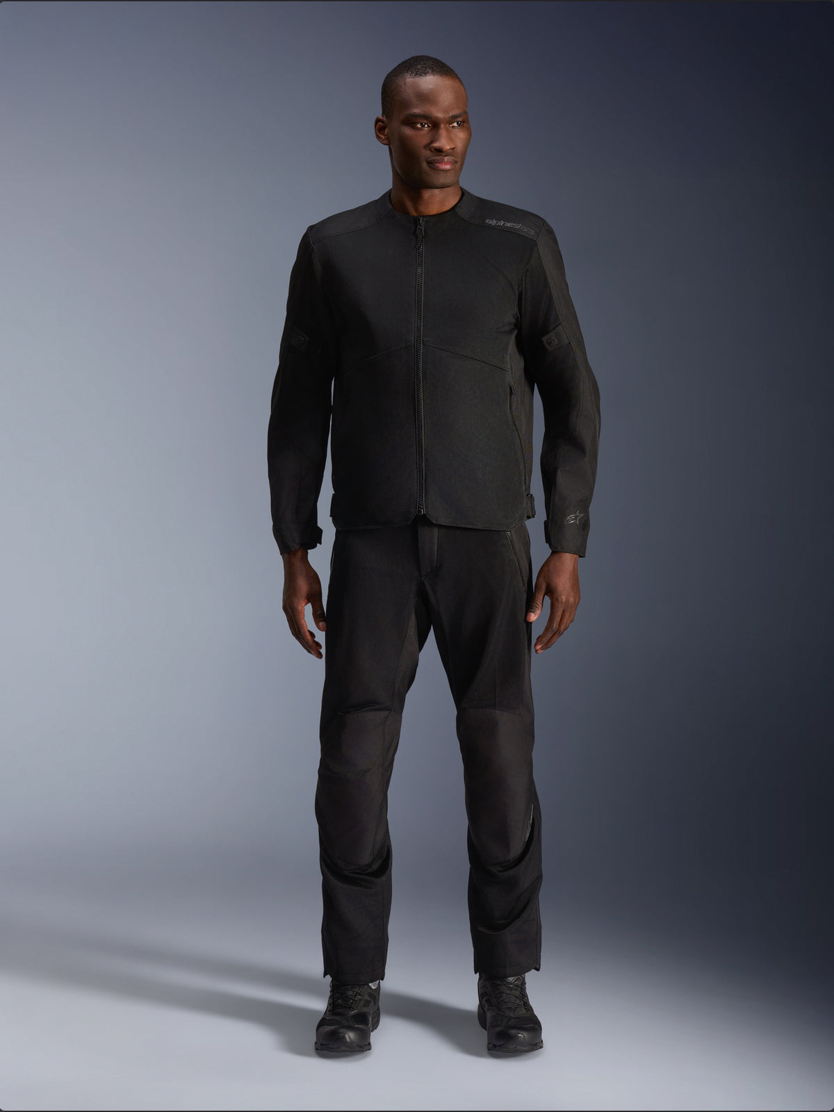 Mannequin homme portant la veste Alpinestars C-1 Air en noir, associée à un pantalon et des bottes noirs assortis, équipement de moto urbain conçu pour les trajets quotidiens, esthétique épurée avec panneaux en maille et marquage discret