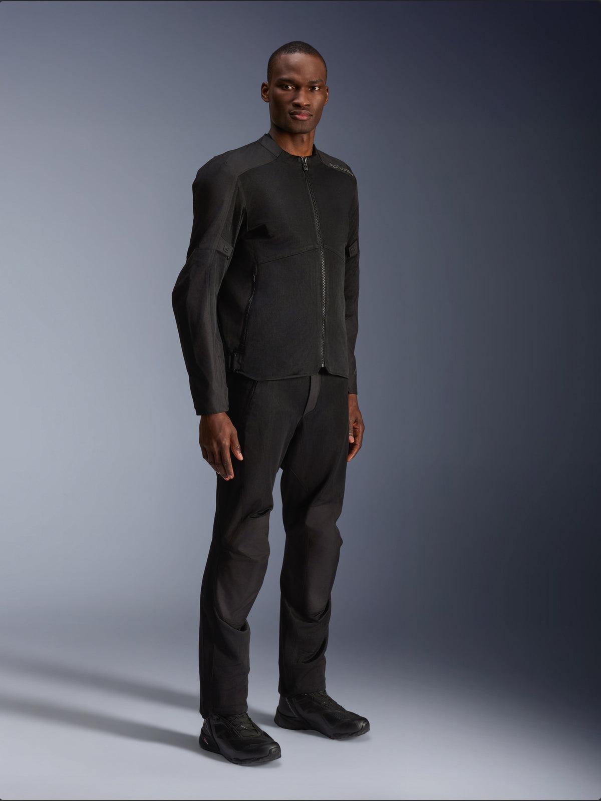 Veste Alpinestars C-1 Air, noir, portée par un mannequin avec pantalon et chaussures de moto noirs assortis, dotée de larges panneaux en maille technique pour la circulation de l'air, esthétique urbaine épurée avec une coupe profilée