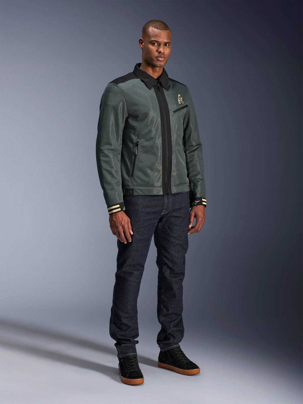 Veste Alpinestars Ignite Air, Urban Gray Black Blue, veste de moto urbaine, portée par un mannequin avec un jean en denim foncé et des baskets noires, dotée d'un corps en maille, d'un col de chemise traditionnel, d'une silhouette inspirée de la veste Harrington et d'un logo Alpinestars doré.