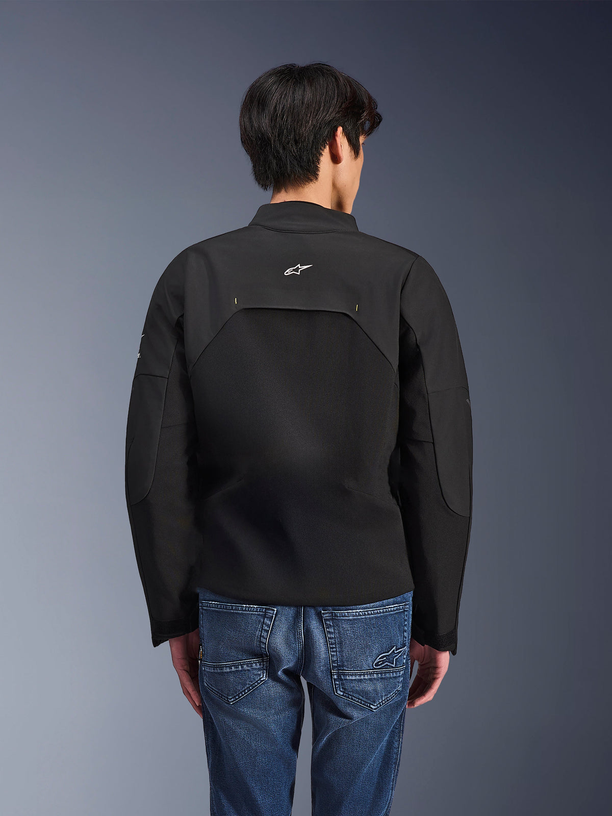 Veste Alpinestars Provoke, veste de moto urbaine, noire, vue arrière montrant le logo Astars blanc et des panneaux techniques en ripstop, portée avec un jean bleu, design contemporain pour les trajets urbains