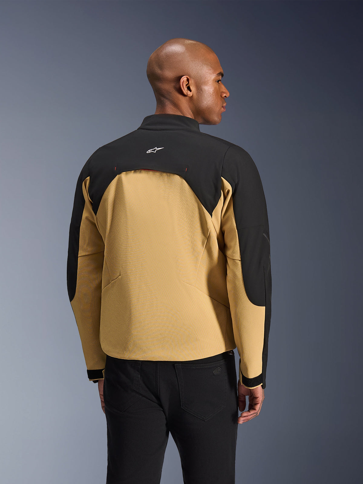 Veste Alpinestars Provoke, veste de moto urbaine, noir et camel, vue arrière montrant la construction bicolore, panneau de ventilation arrière doublé en mesh, petit logo blanc sur le haut du dos, portée avec un pantalon noir